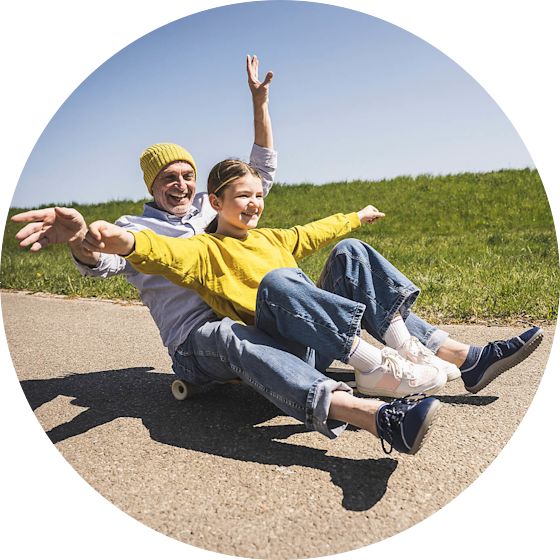 Mit dem Kombitarif Strom und Gas bis du günstiger unterwegs Vater und Tochter sitzen zusammen auf einem Skateboard und fahren den Berg lachend herunter