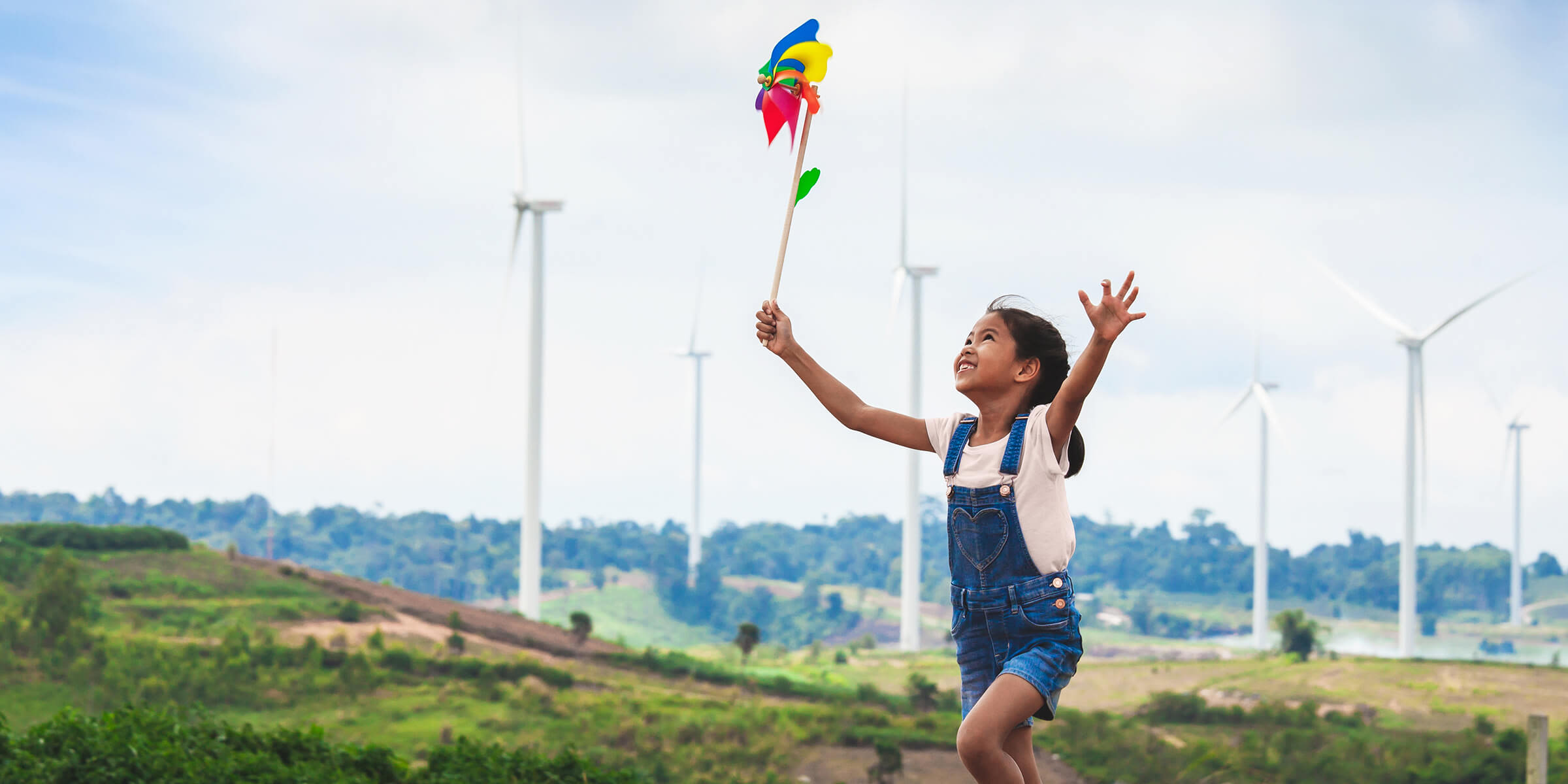 Mehr als grüne Energie: Energiewende einfach erklärt. Mädchen läuft mit buntem Windrad durch einen Windpark.