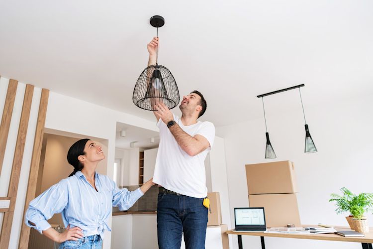 Junges Paar hängt Lampe im Wohnzimmer auf