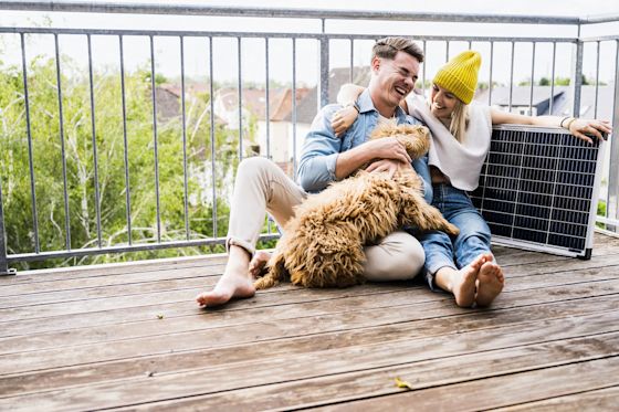 Du hast nicht das passende Solardach? Balkonsolar ist eine einfache Alternative Mann und Frau auf Balkon mit Hund und Solarpanel.