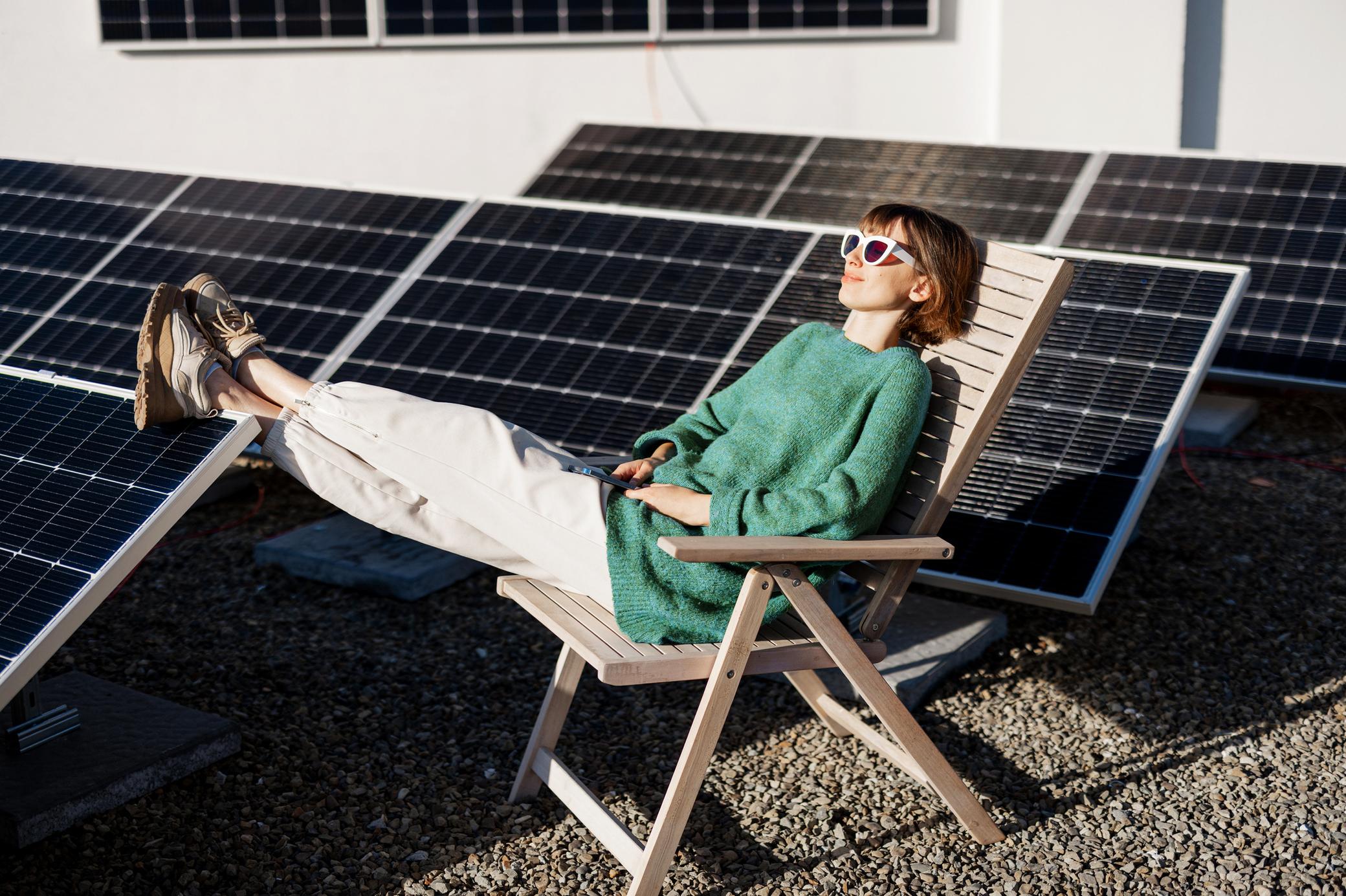 Frau liegt entspannt auf einem Holzstuhl auf einem Flachdach mit Solaranlage
