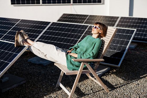 Solaranlagen gibt es auch für dein Flachdach Frau liegt entspannt auf einem Holzstuhl auf einem Flachdach mit Solaranlage