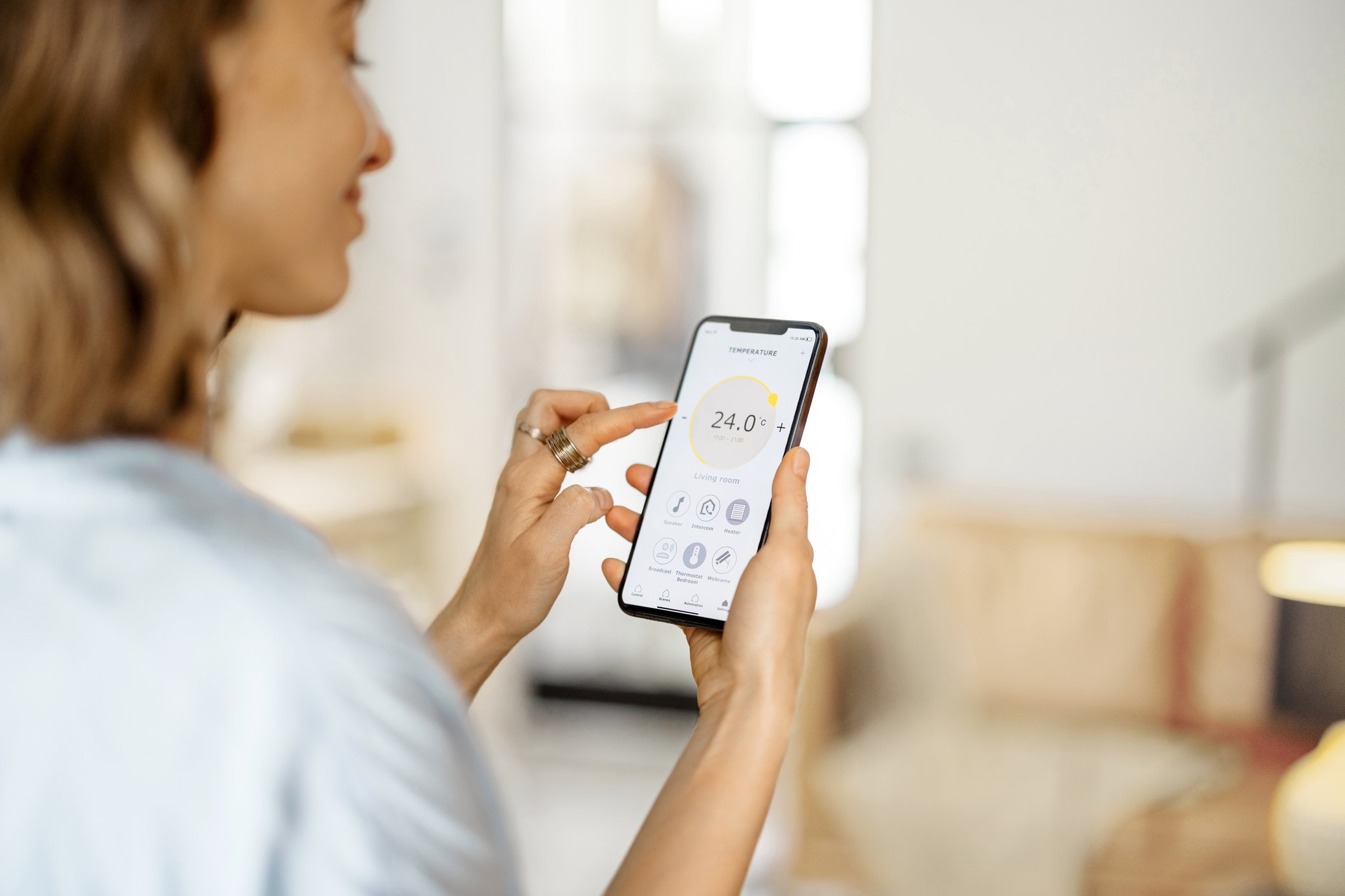 Frau passt in einer Smart-Home-App auf ihrem Handy die Zimmertemperatur an