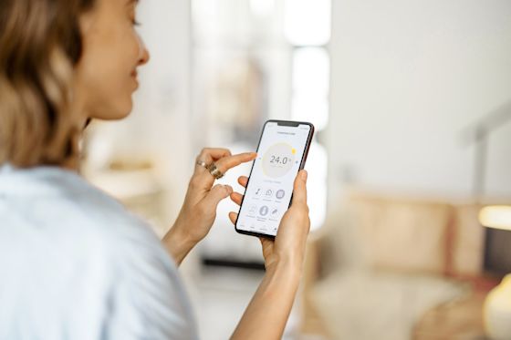 Mit Smart-Home-Anwendungen sparst du zuhause einfach Energie Frau passt in einer Smart-Home-App auf ihrem Handy die Zimmertemperatur an