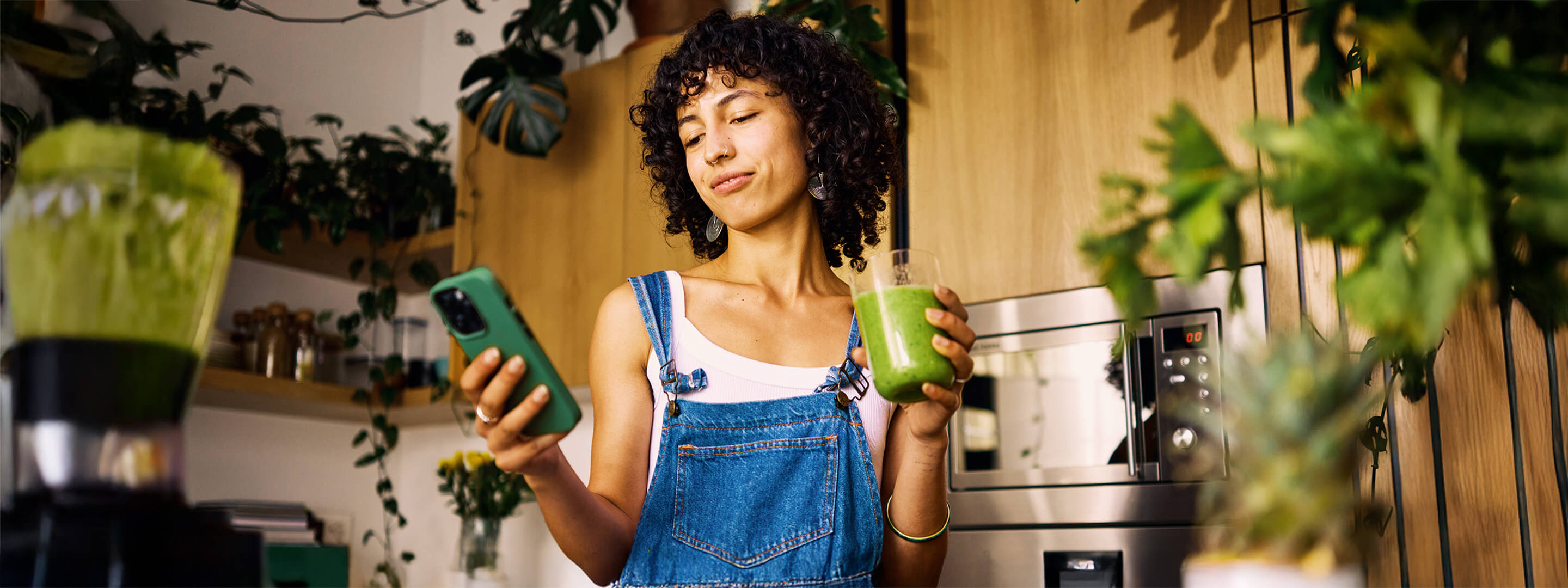 Mach dir deinen eigenen Strommix - am besten grün Frau mit Smoothie in der Hand steht in der Küche und schaut auf ihr Smartphone