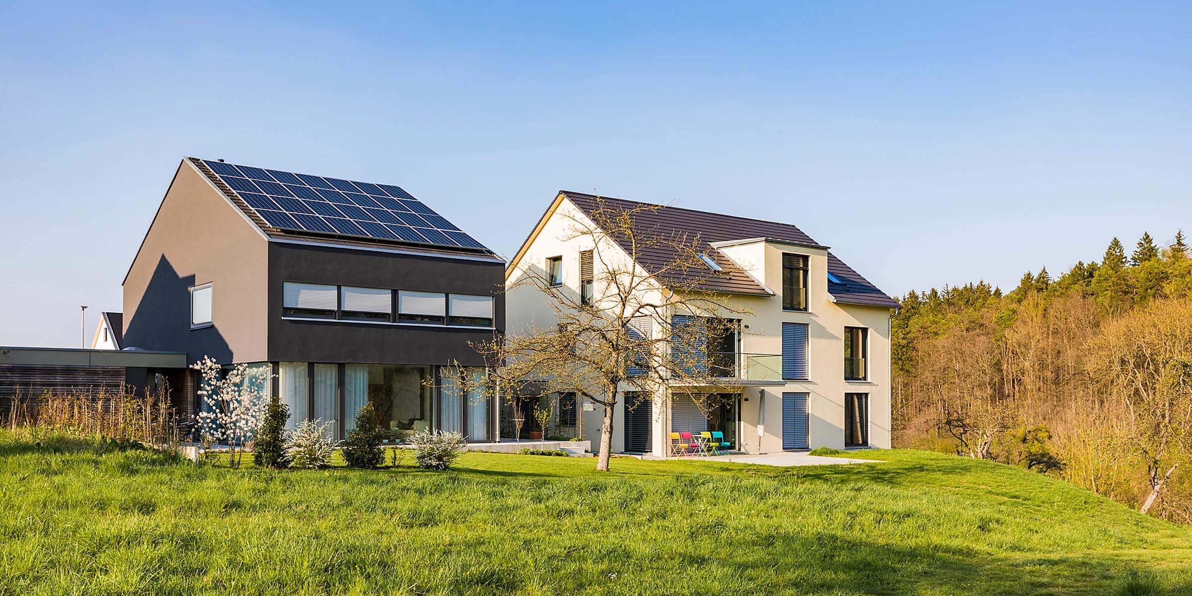 Modernes Einfamilienhaus mit Photovoltaik-Anlage steht neben Haus ohne Photovoltaik-Anlage