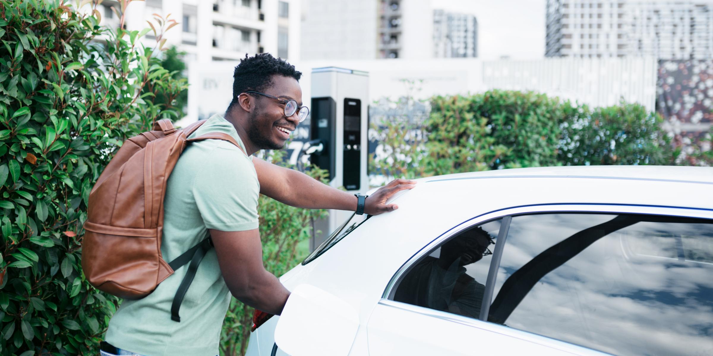 Ein Mann mit Rucksack lädt sein E-Auto an einer öffentlicher Ladesäule