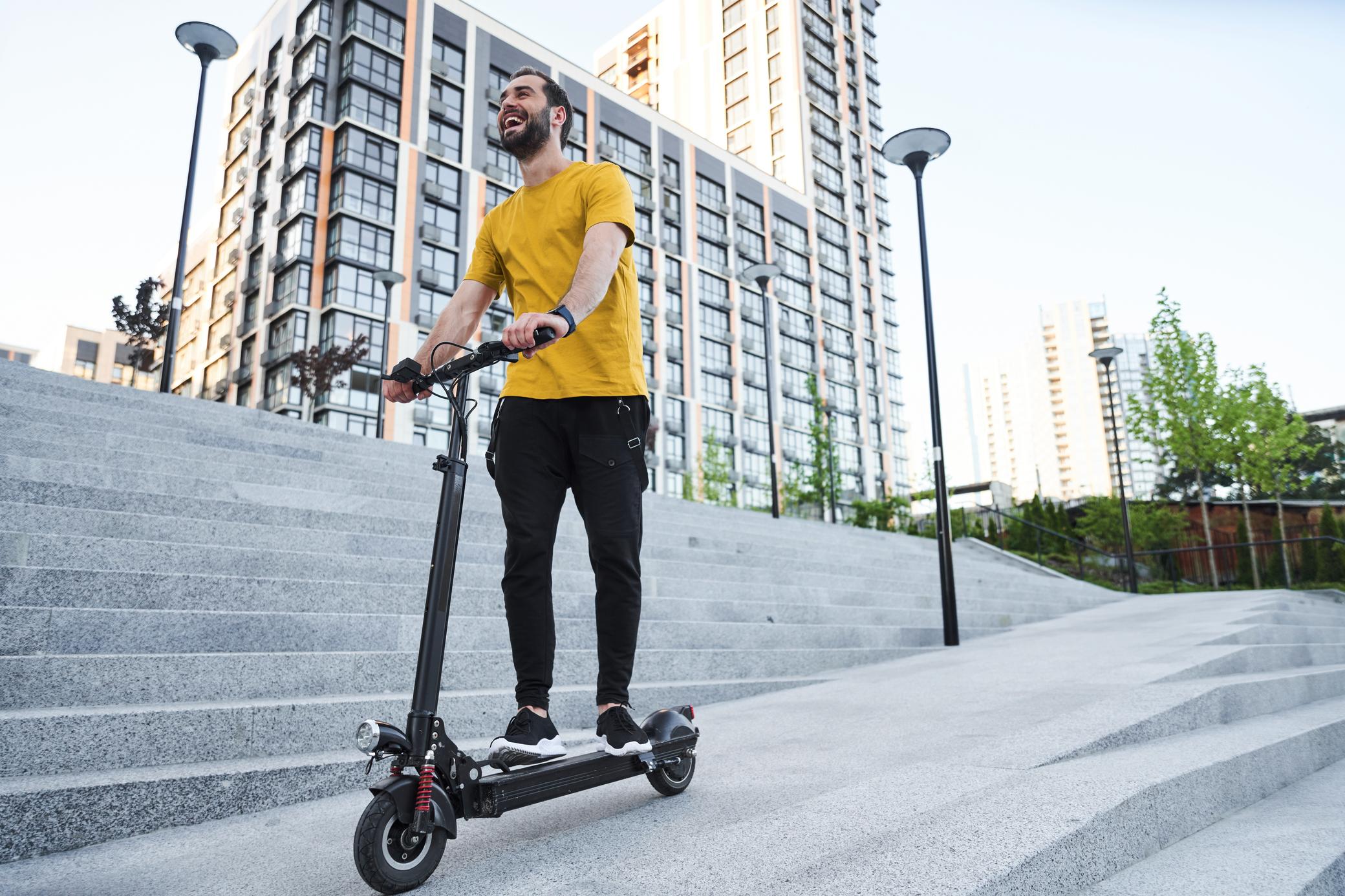 Mann trägt ein gelbes Shirt und fährt auf einem E-Scooter.