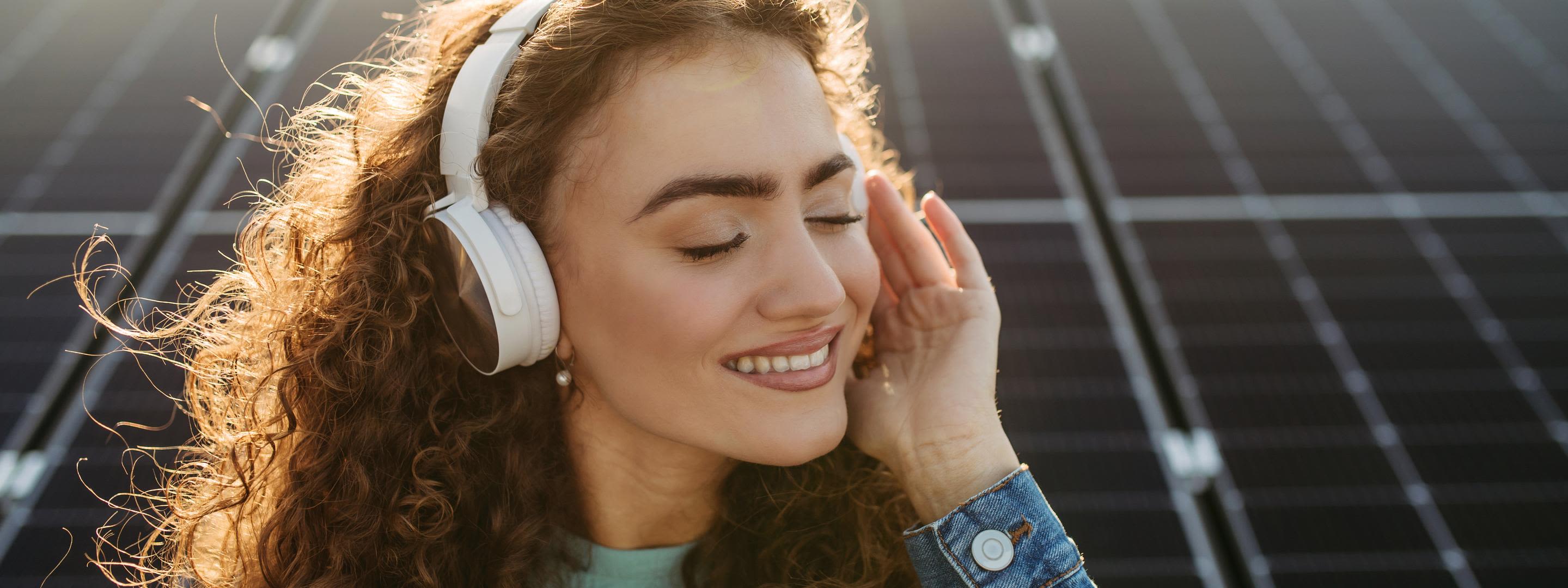 Kosten einer Solaranlage für das eigene Zuhause Frau mit Kopfhörern hört Musik vor Solaranlage