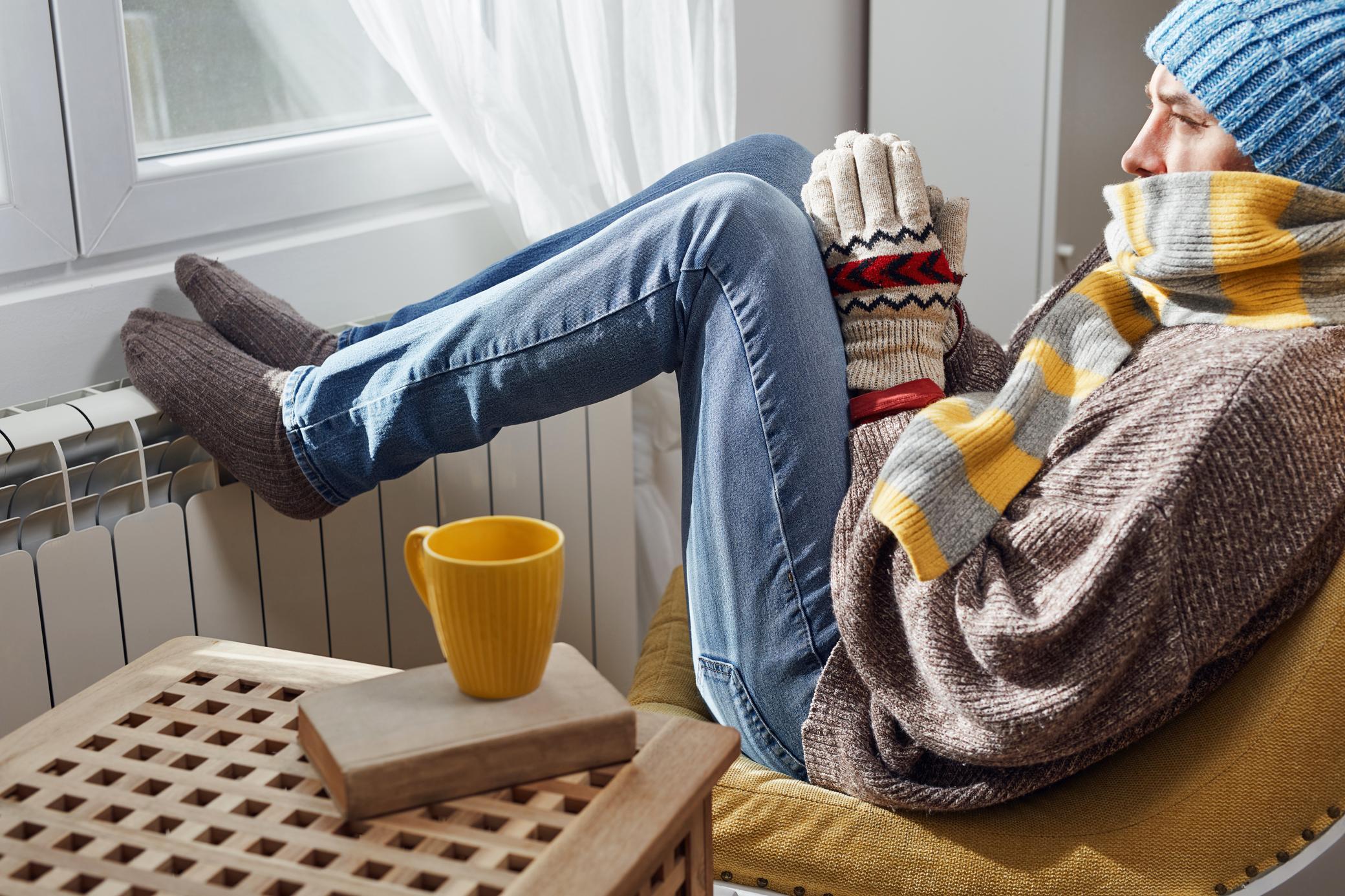 Mann in warmer Kleidung wärmt sich am Heizkörper