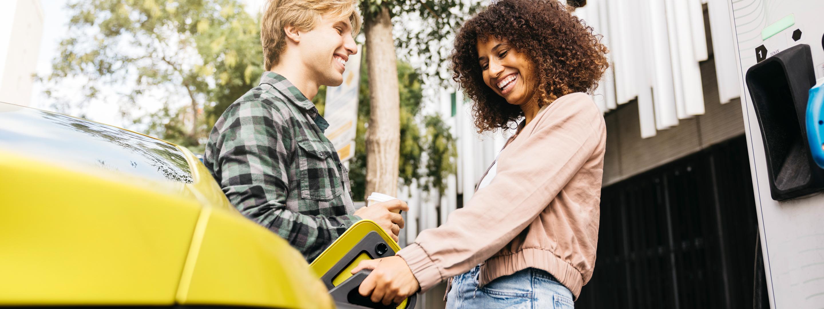 Mit der THG-Quote fährst du dein E-Auto noch günstiger Junges Paar lädt lachend ihr gelbes E-Auto in der Stadt auf
