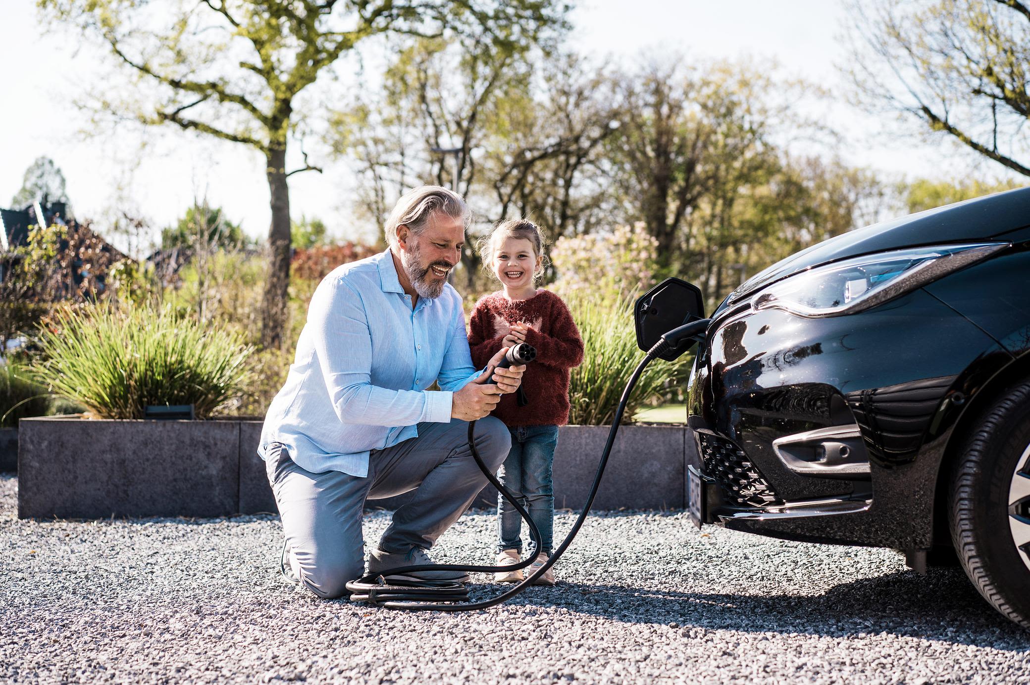 Mit einem E-Auto und Wallbox zieht meist ein Smart Meter mit ein Vater und Tochter laden ein E-Auto mit Ladestecker zuhause
