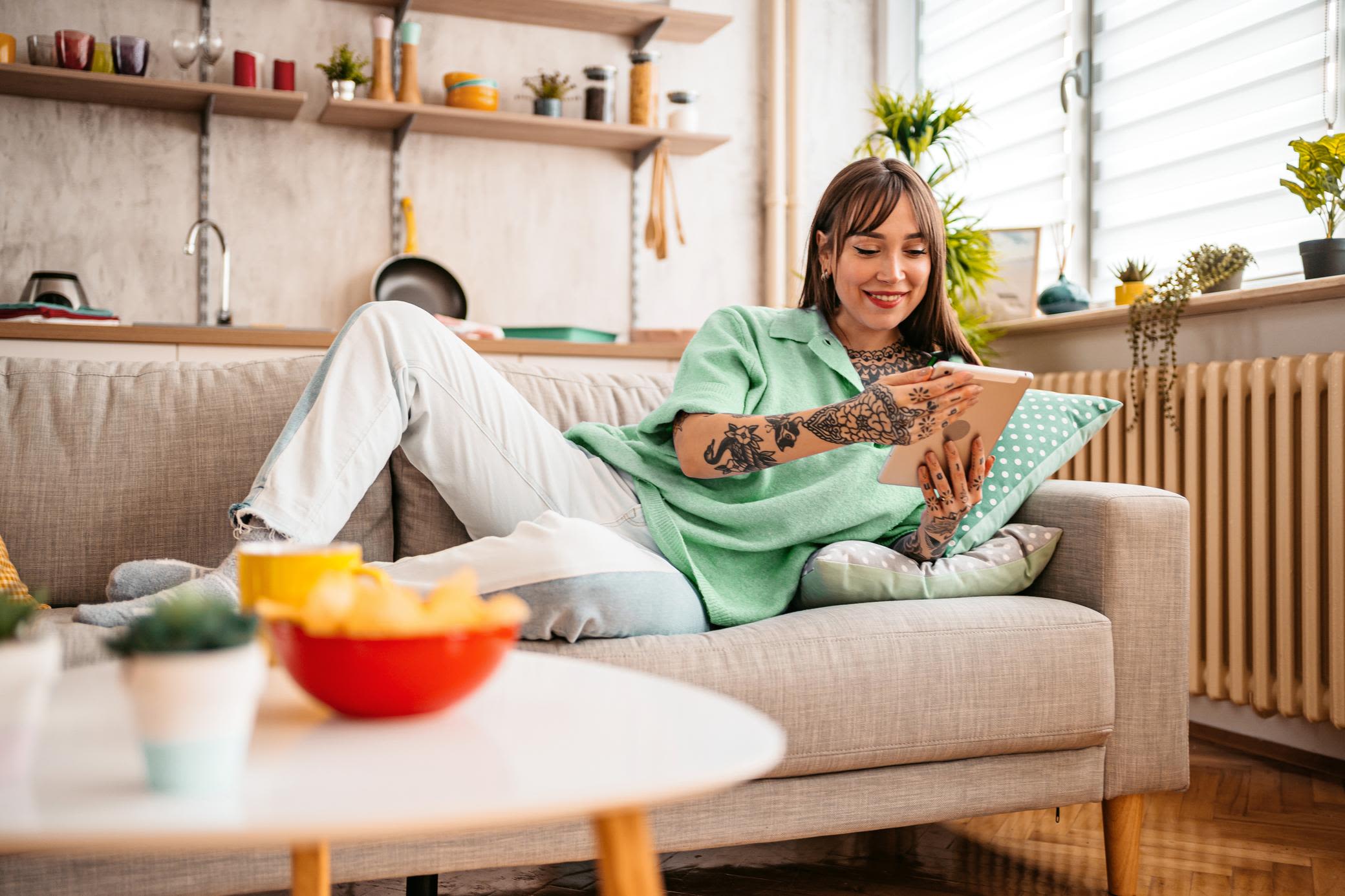 Strom und Energie muss nicht kompliziert sein - Digital geht's einfach Junge Frau auf dem Sofa steuert mit dem Tablet ihre Smart-Home-Geräte