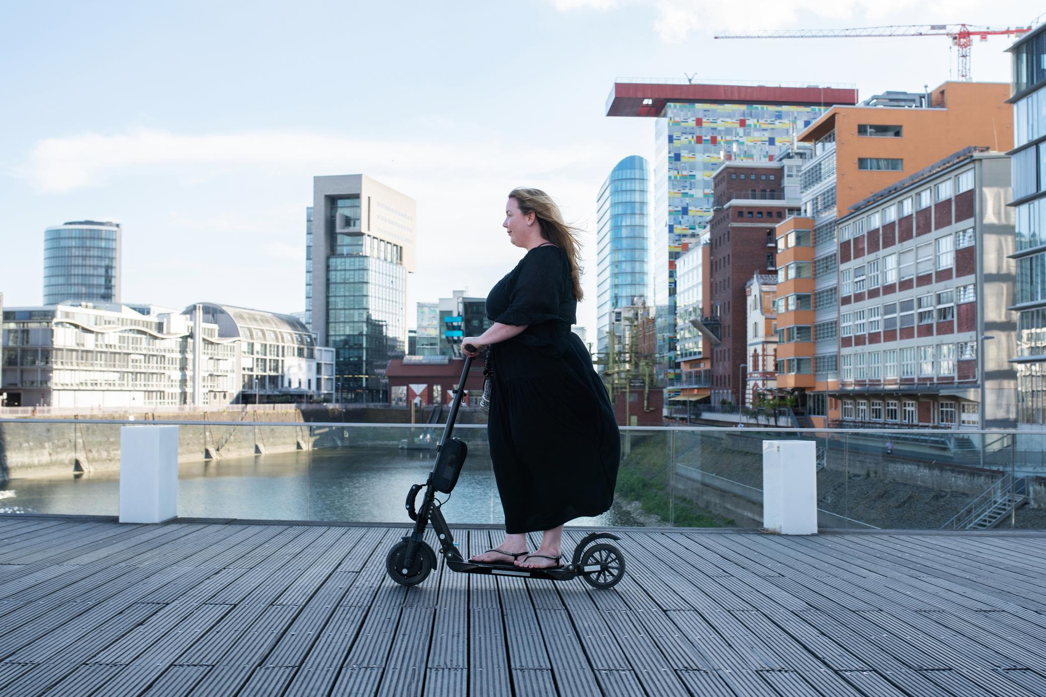 Mit E-Scooter kommst du einfach schneller in der Stadt voran Frau mit schwarzem Kleid rollt auf E-Scooter durch den Rheinhafen in Düsseldorf