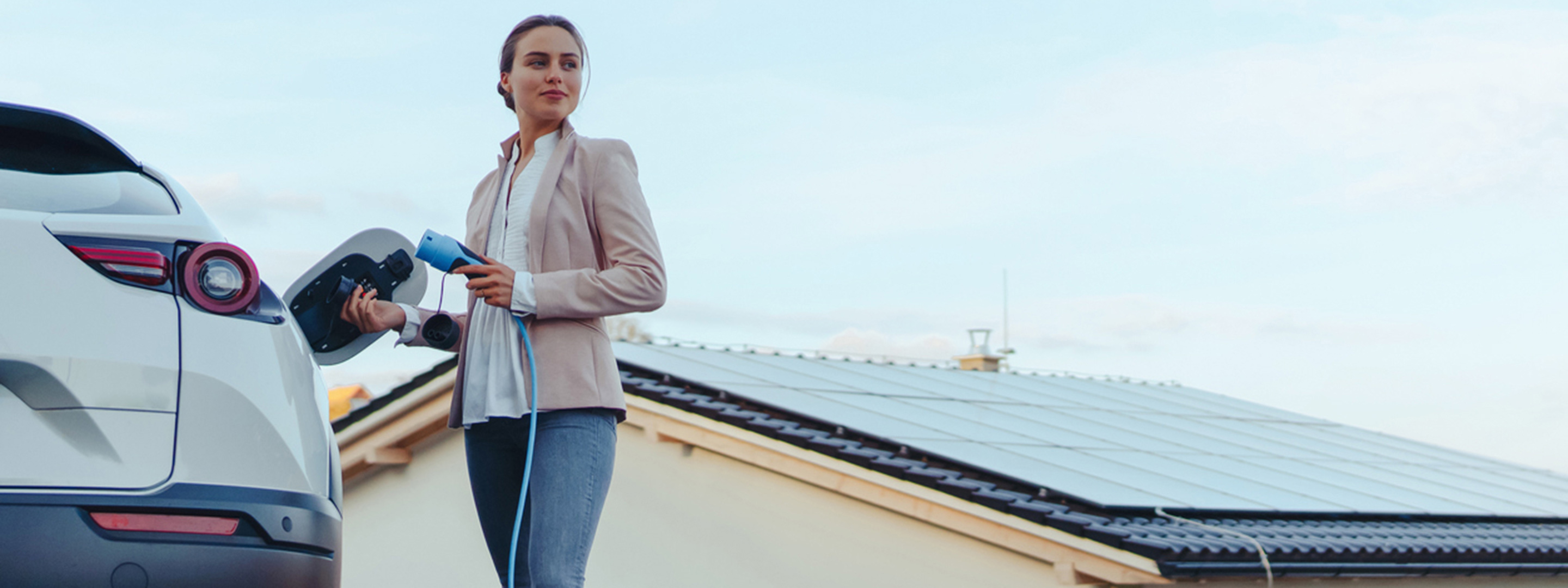Frau lädt ihr E-Auto - mit eigener Solaranlage auf dem Dach