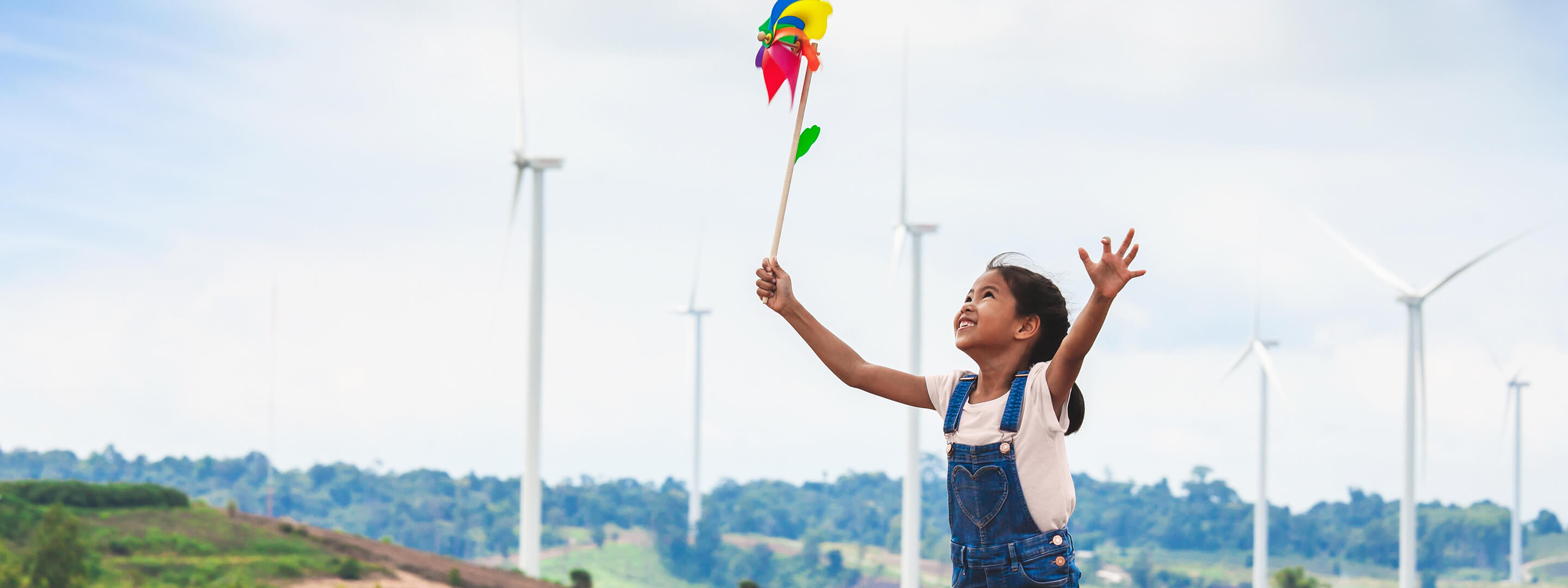 Mädchen läuft mit buntem Windrad durch einen Windpark