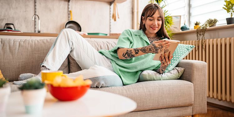 Mach dir dein Zuhause smart mit kleinen digitalen Helfern Junge Frau auf dem Sofa steuert mit dem Tablet ihre Smart-Home-Geräte