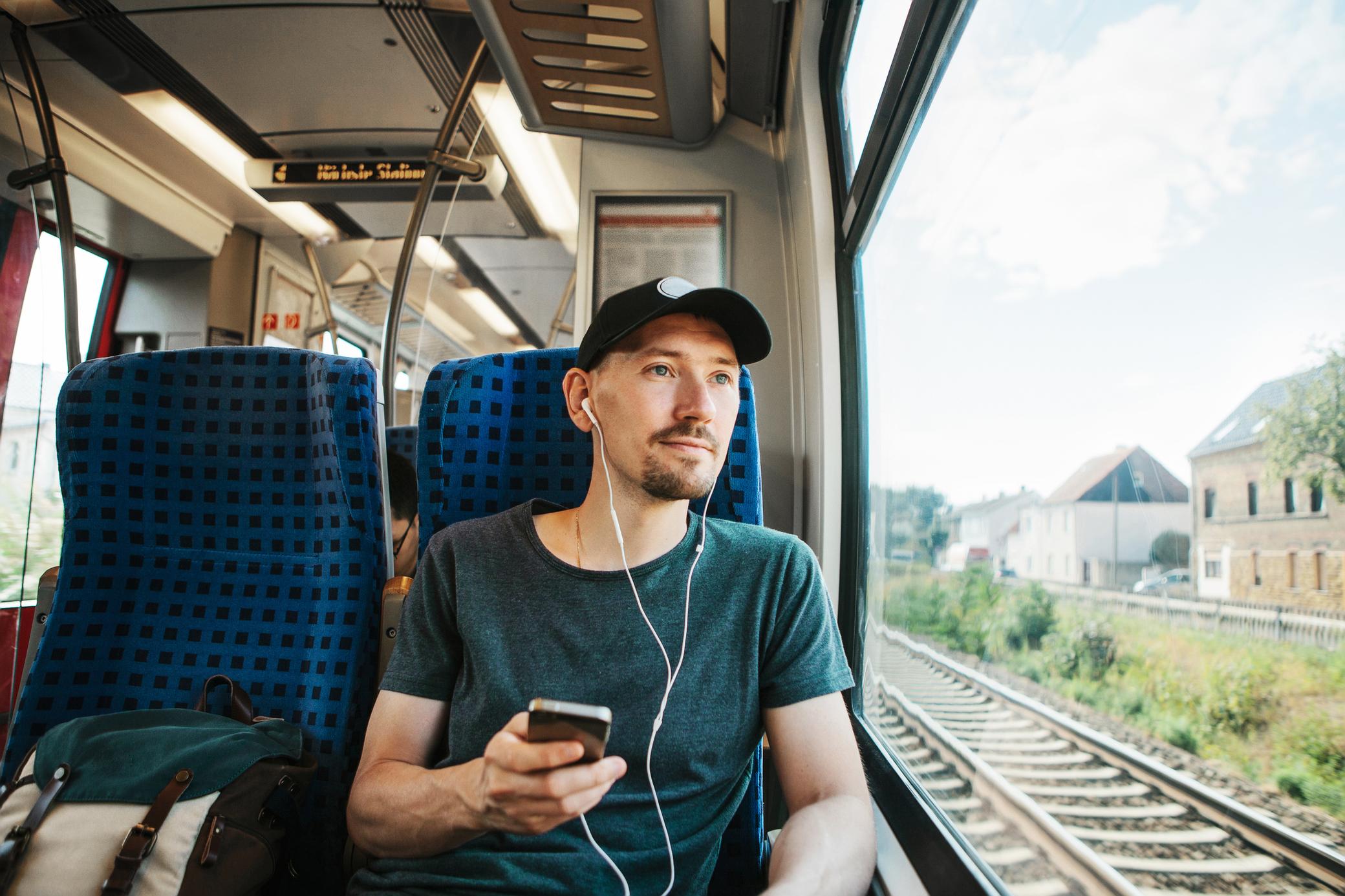 Junger Mann mit Kappy und Handy fährt im Zug