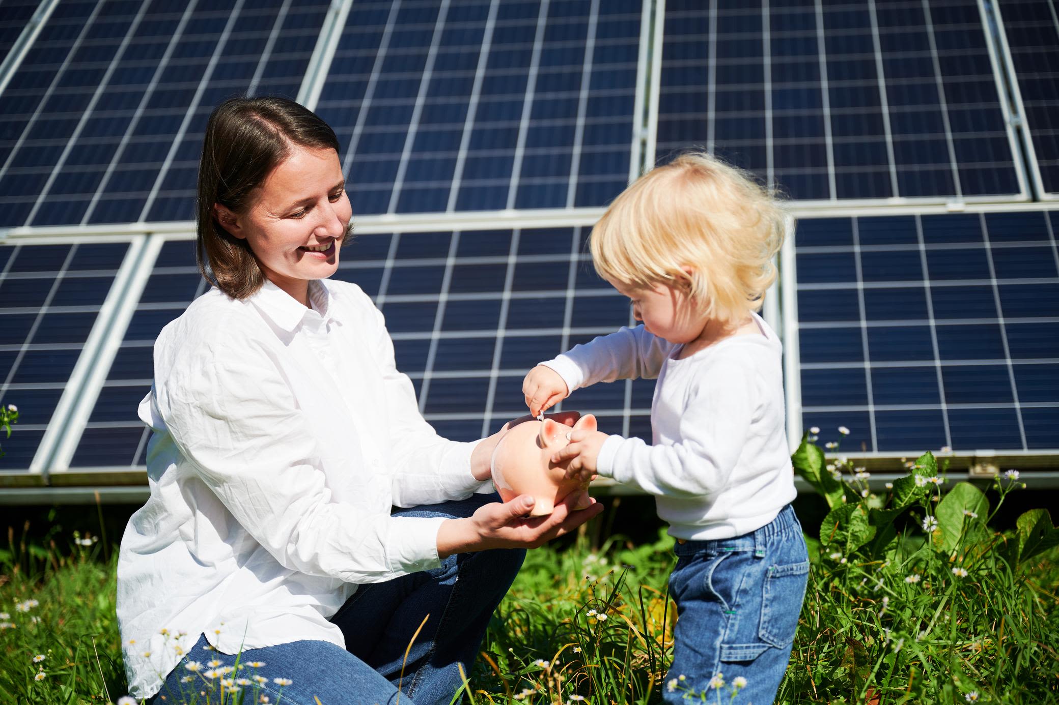 Mit einer eigenen Solaranlage Stromkosten sparen Frau mit Kind und Sparschwein vor einer Solaranlage