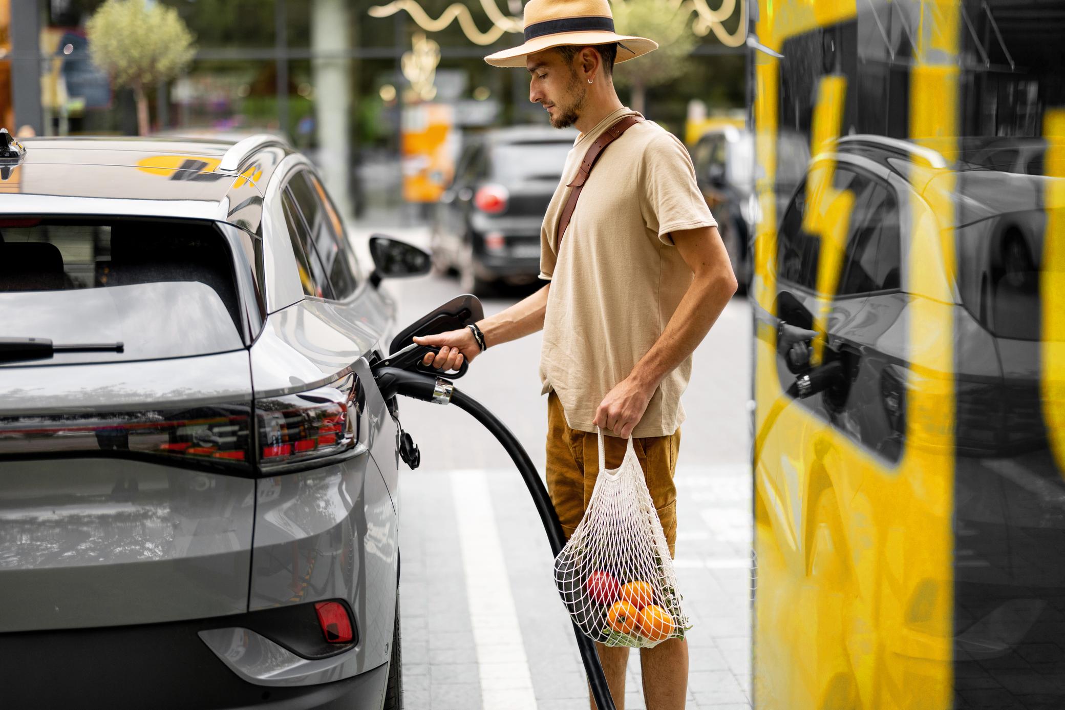 Junger Mann lädt sein Elektroauto an öffentlicher Ladesäule auf