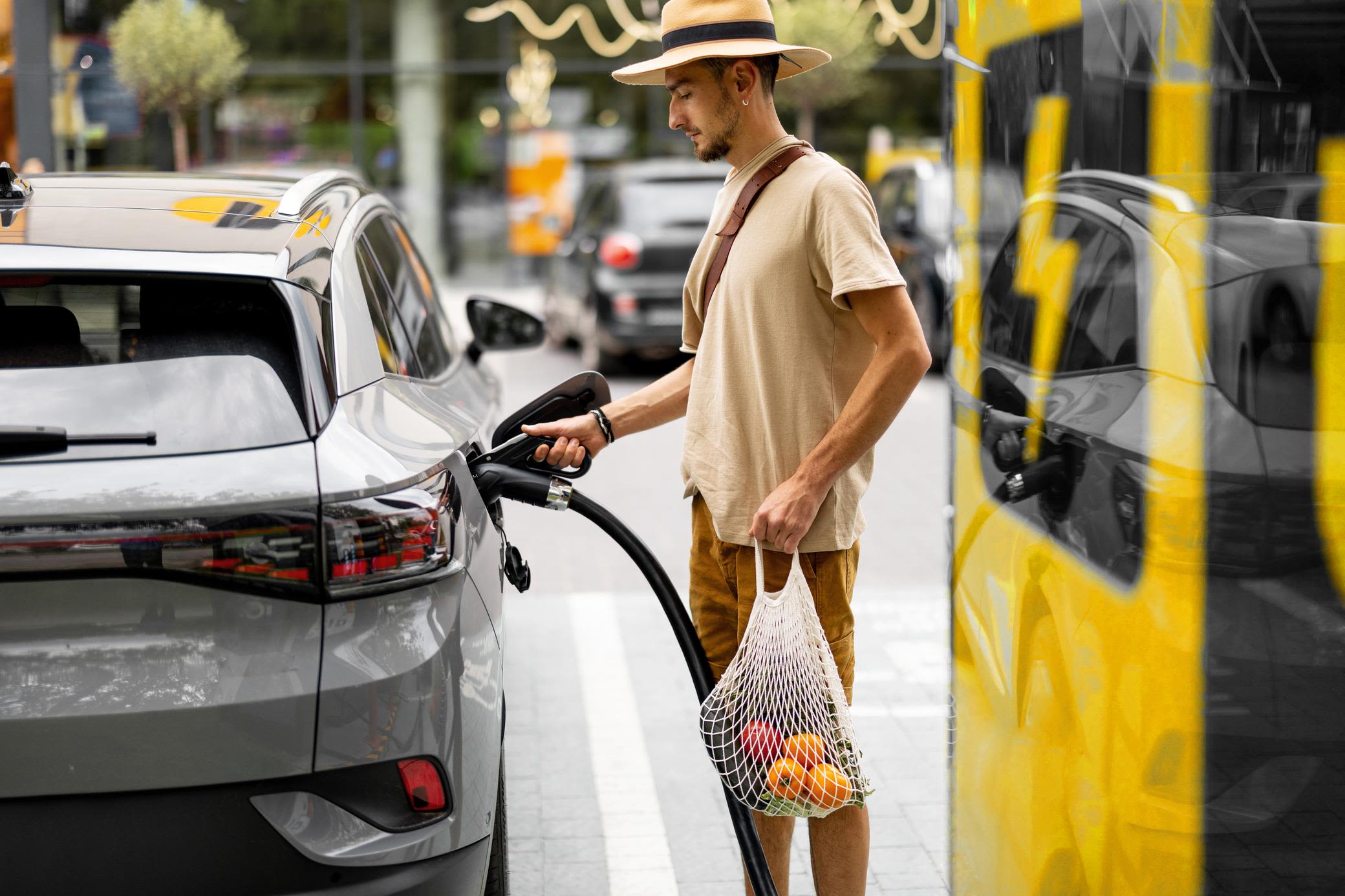 E-Autos werden mit Wechselstrom aufgeladen Junger Mann lädt sein Elektroauto an öffentlicher Ladesäule auf