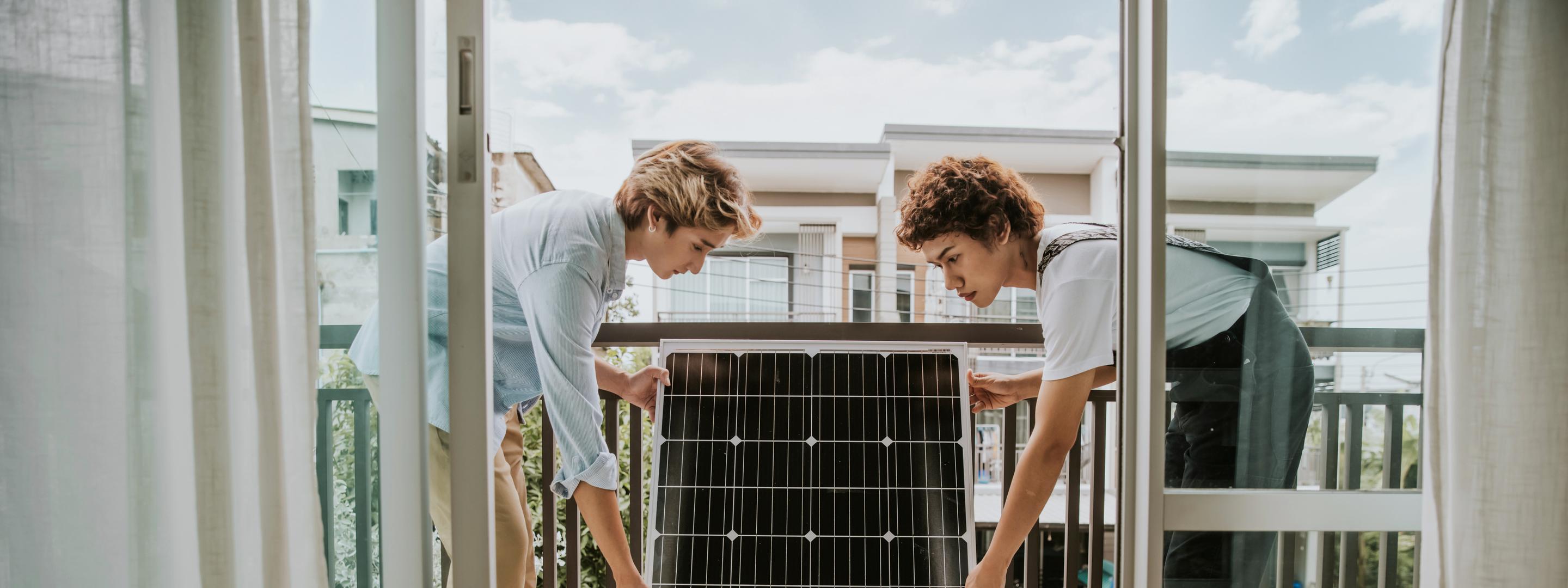 Zwei junge Frauen installieren ein Solarmodul auf dem Balkon
