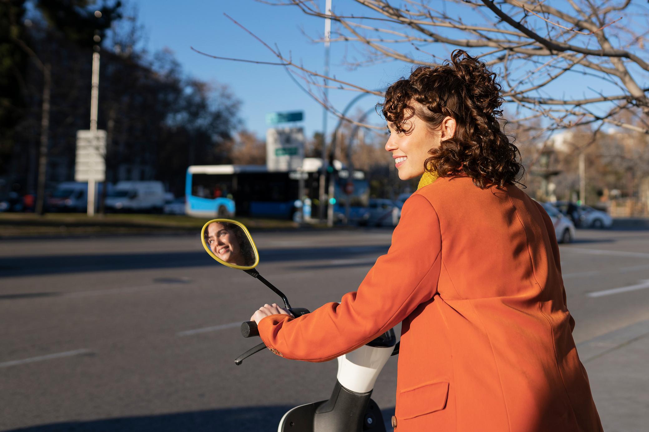 Frau in roter Jacke fährt auf E-Roller in der Stadt