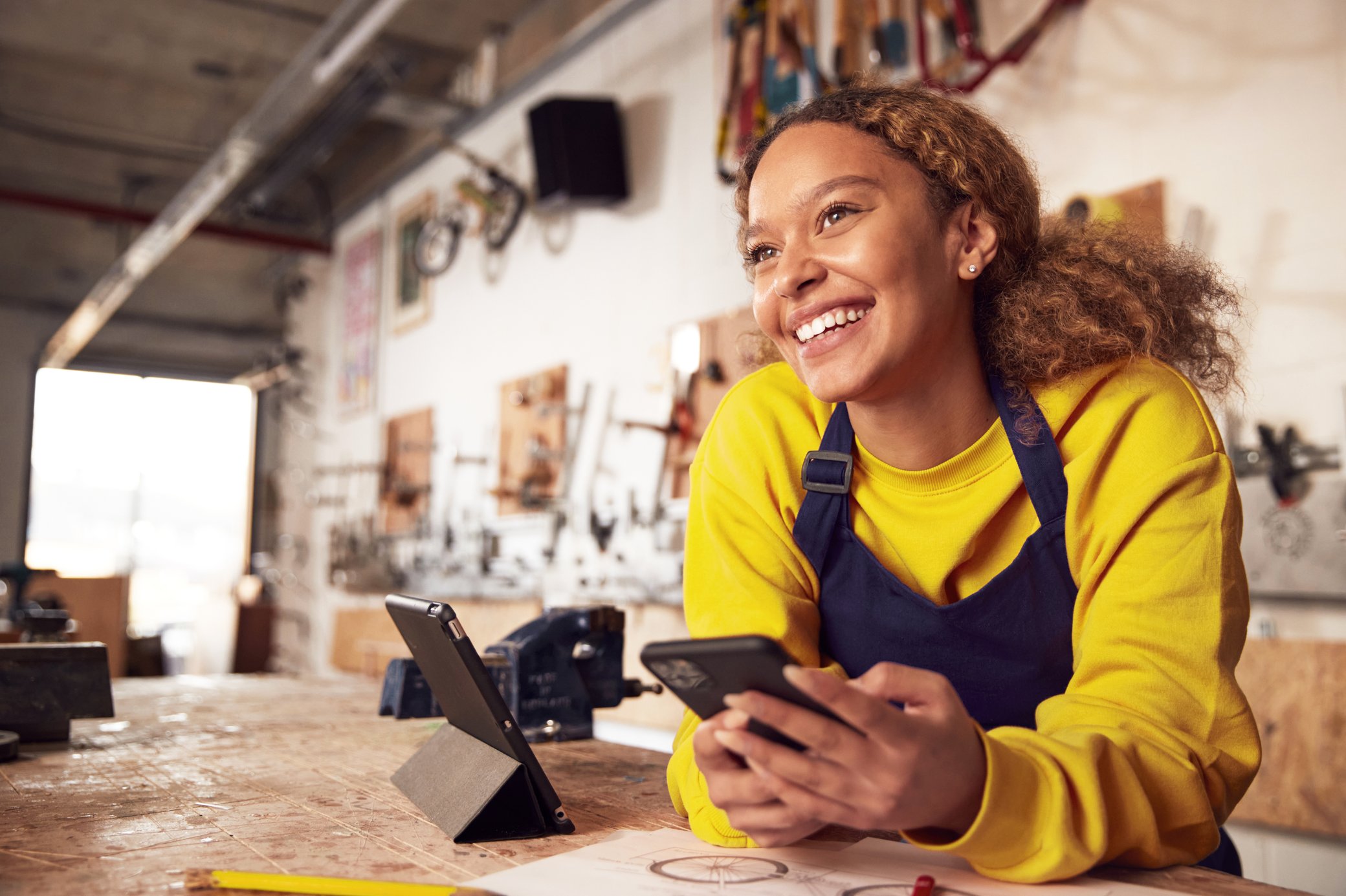 Frau mit einem Handy in der Hand arbeitet in einer Werkstatt