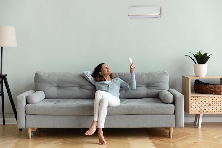 Wärmetauscher kommen in einer Klimaanlage zum Einsatz Frau sitzt auf der Couch un bedient eine Klimaanlage