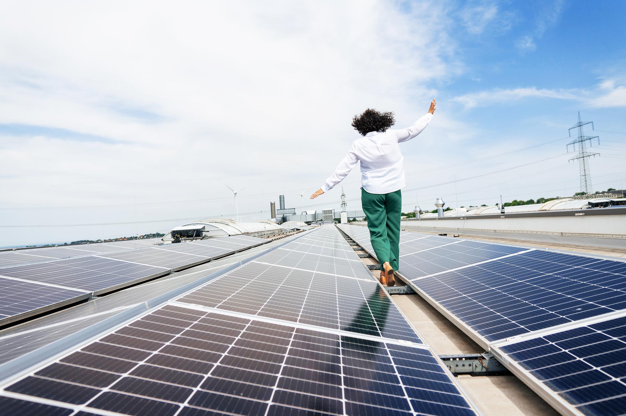 Frau balanciert barfuß auf einem Flachdach mit Solaranlage