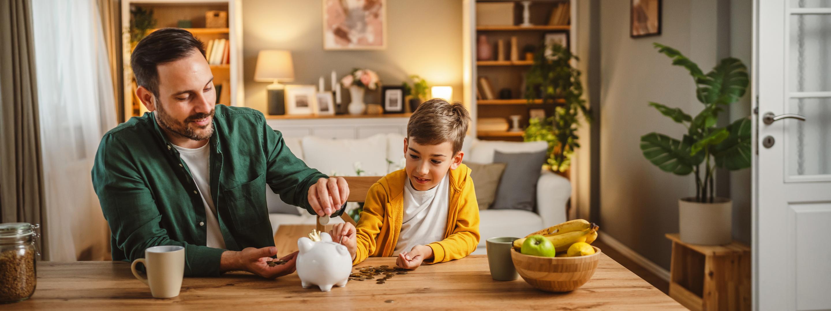 Vater und Sohn sitzen am Tisch im Wohnzimmer und füllen Sparschwein auf