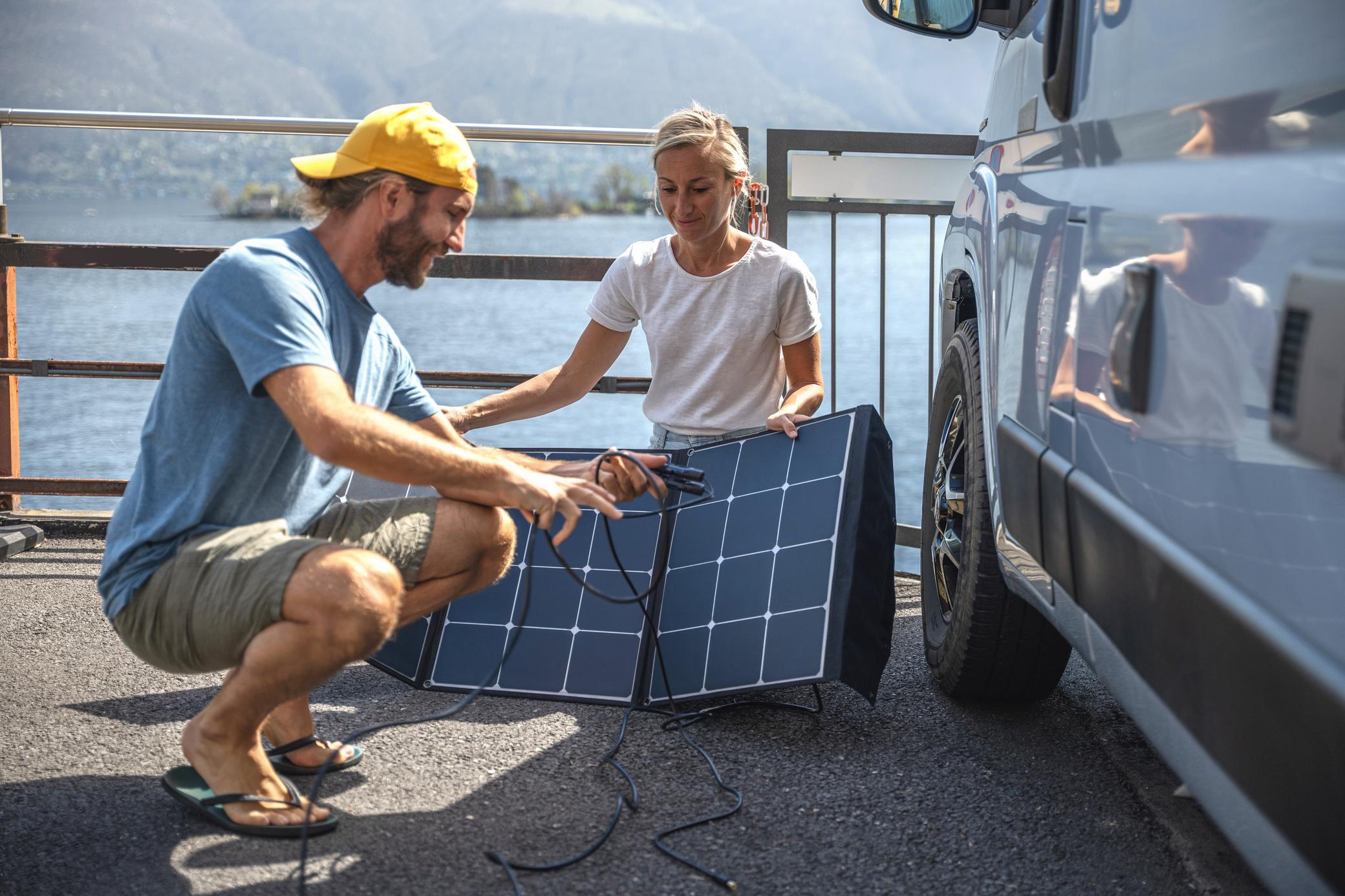 Junges Paar mit faltbarem Solarpanel neben ihrem Camper Van
