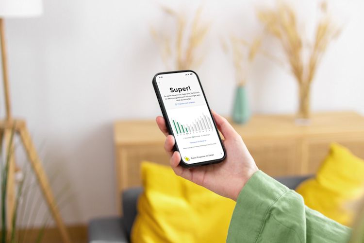 Zuhause smart Energie sparen per App: Verbrauch und Kosten immer im Blick haben macht Spaß Hand einer Frau hält ein Handy mit Yello App und Screen mit Verbrauchsverlauf im grünen Balkendiagramm
