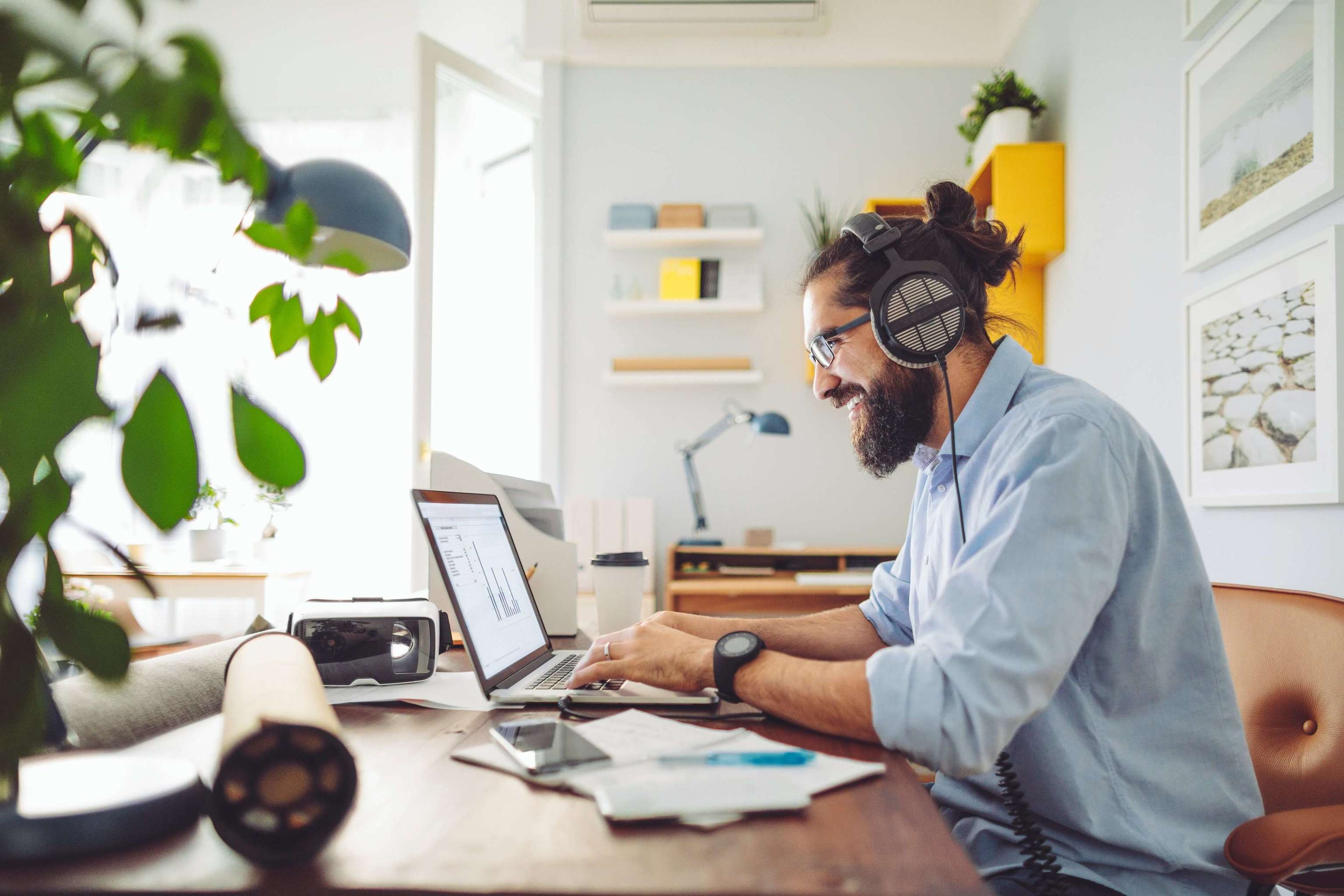 Mann mit Kopfhörern sitz mit einem Laptop am Schreibtisch Mann mit Kopfhörern sitz mit einem Laptop am Schreibtisch