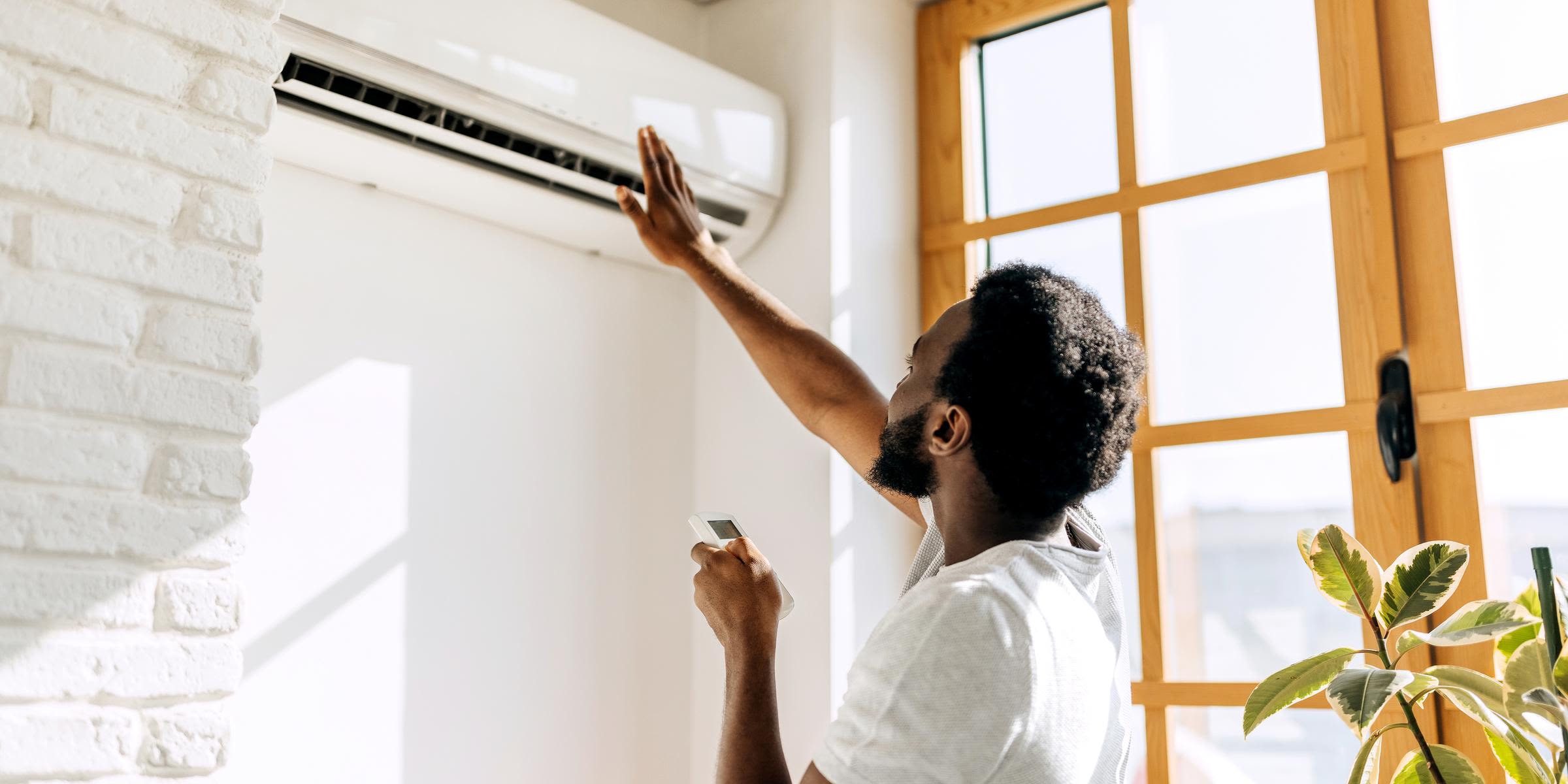Mit einer Klimaanlage Zuhause durch den heißen Sommer Mann in weißem T-Shirt und Fernbedienung prüft den Luftzug seiner Klimaanlage