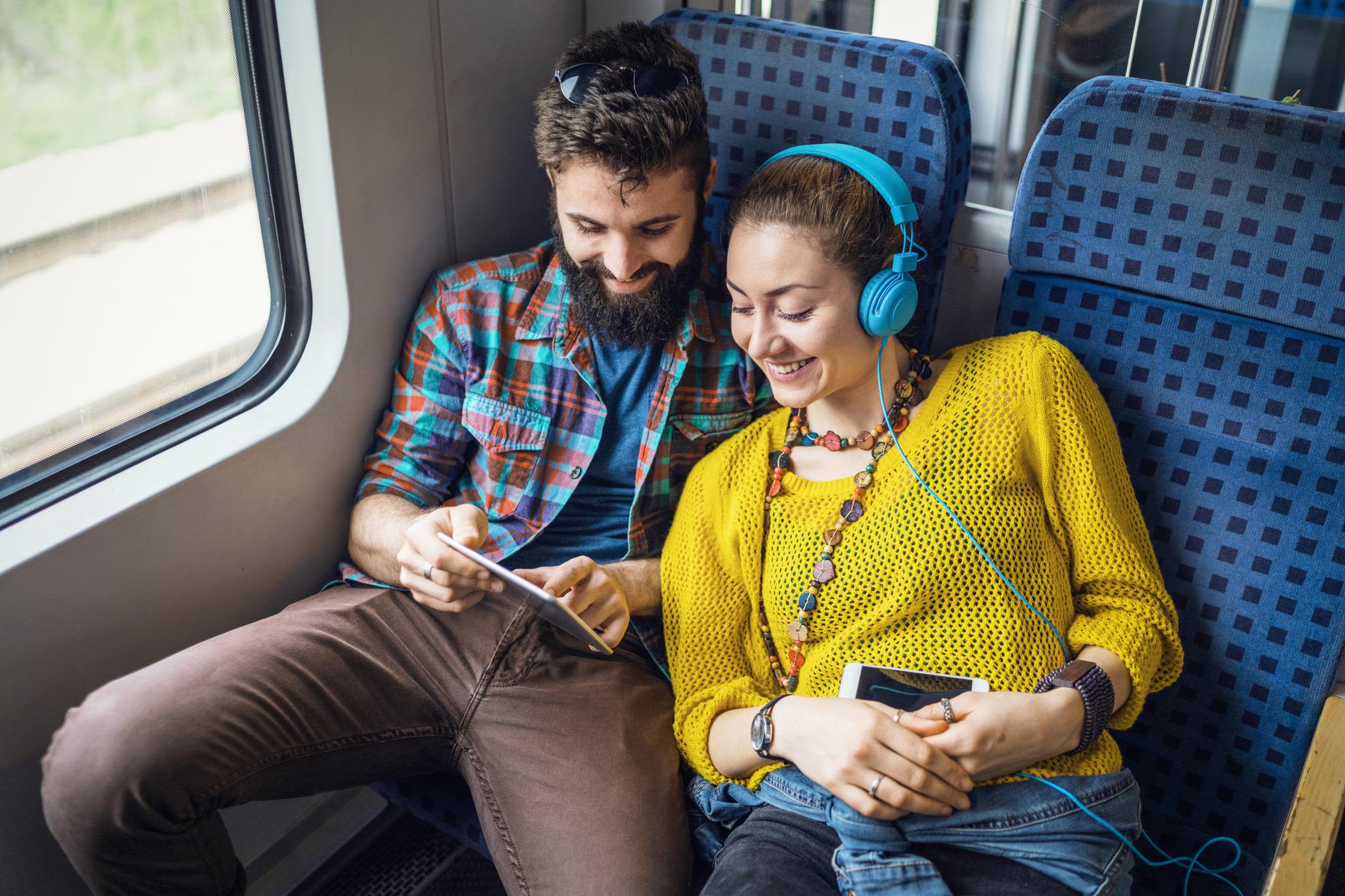 Auch bei der Zugfahrt wird Strom genutzt Glückliches Paar mit Tablet und Handy im Zug