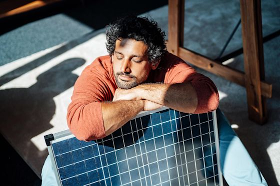 Super praktisch und gut beraten. Das Solarangebot für Miete oder Kauf über Yello Mann mit orangem Pullover lehnt entspannt auf einem Solarmodul