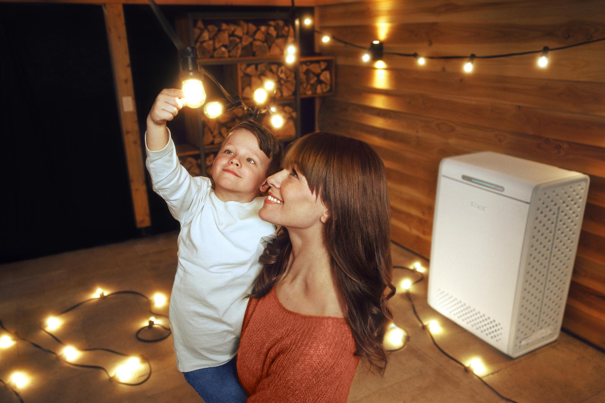 Mit einem Stromspeicher verbrauchst du mehr Solarstrom selbst Mutter hält Kind, das mit Lichterkette spielt. Im Hintergrund ein Stromspeicher