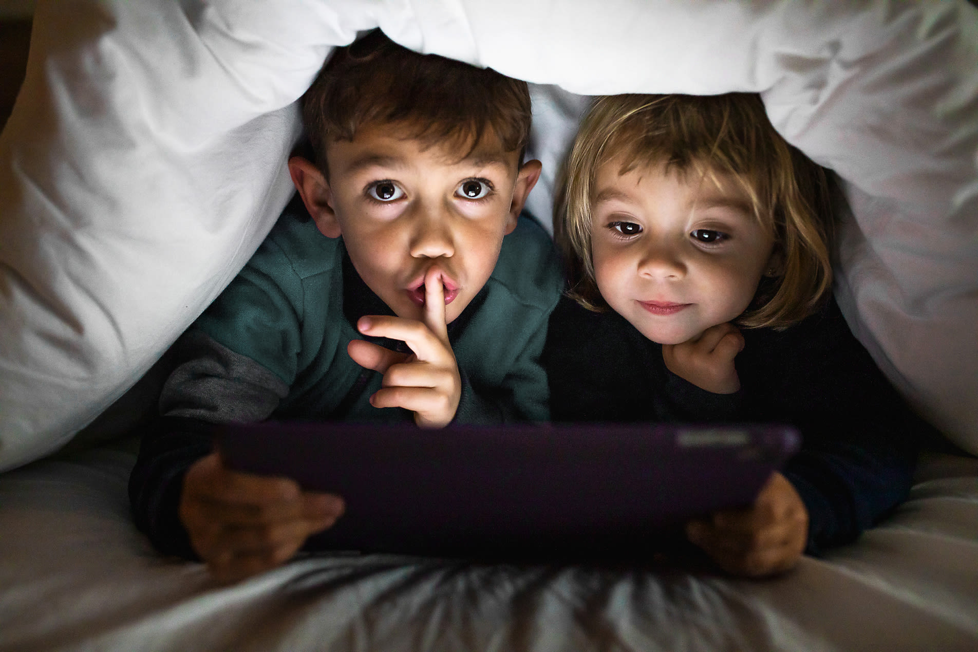 Ein Stromausfall kommt in Deutschland selten vor Geschwister schauen auf Tablet unter einer Decke