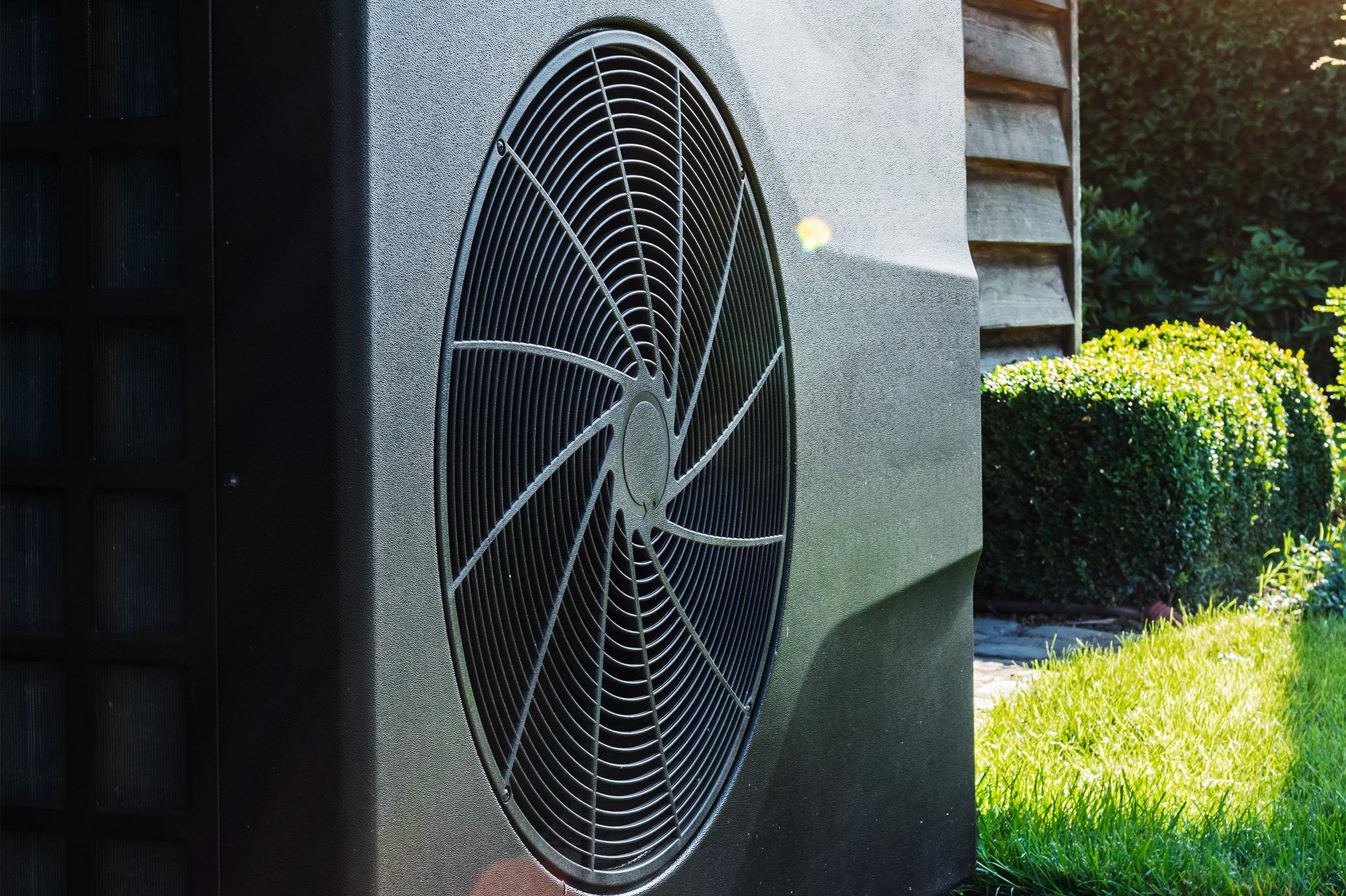 Mit einer Wärmepumpe heizt du dein Zuhause nachhaltig Schwarze Wärmepumpe hinterm Haus im Garten