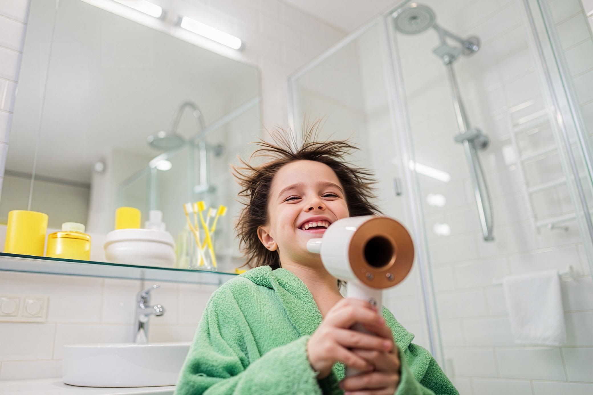 Strom im Alltag: Föhne deine Haare und lass deine Geräte günstig mit Strom versorgen Junge in grünem Bademantel föhnt sich die Haare im Badezimmer