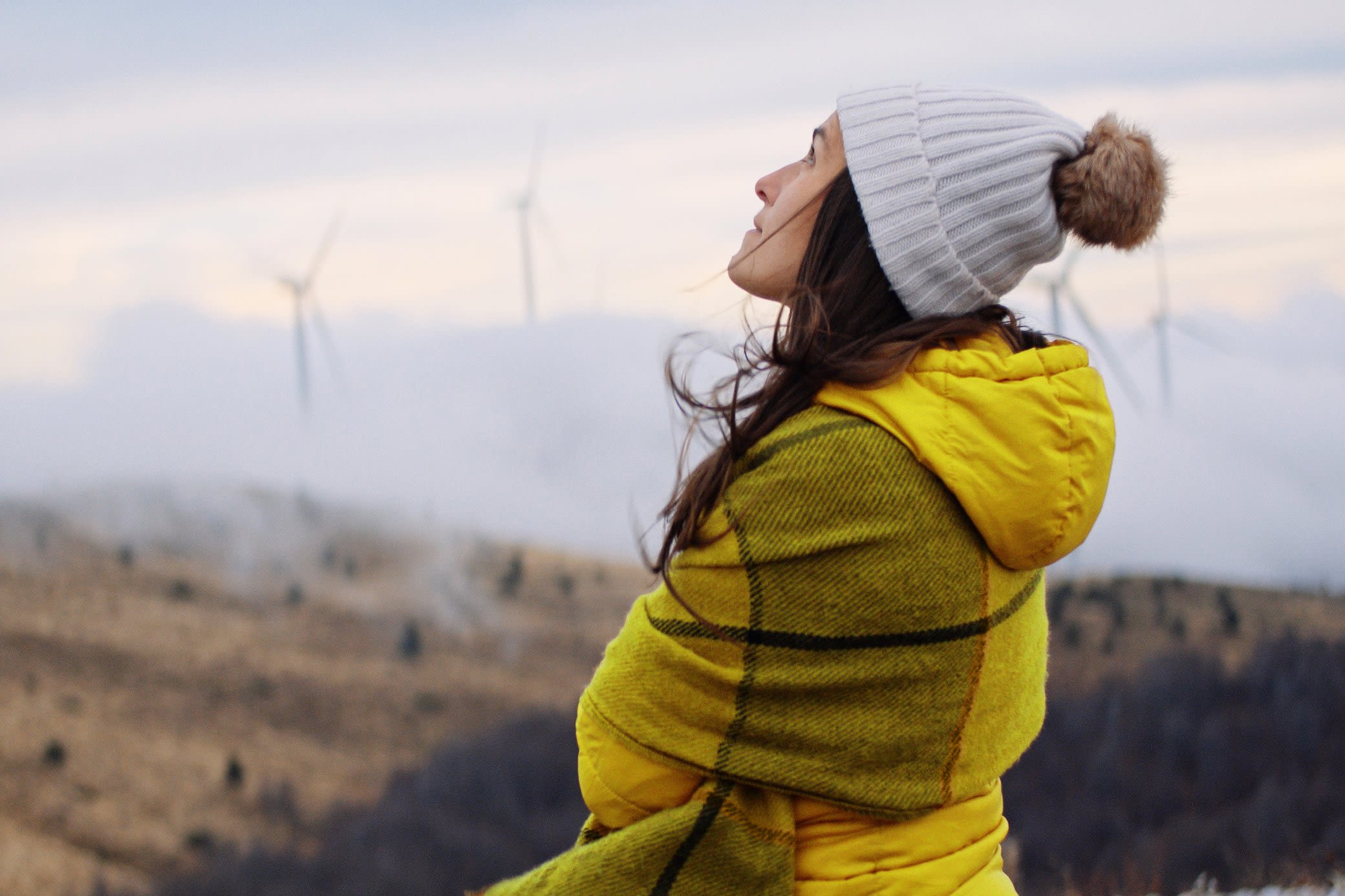 Windenergie macht im Strommix den größten Anteil aus Frau in gelber Winterjacke schaut an einem kalten Tag auf Windkraftanlagen im Hintergrund