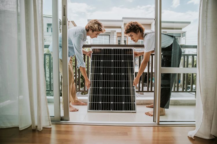 Eine Balkonsolaranlage lässt sich ganz unkompliziert selbst anbringen Zwei junge Frauen installieren ein Solarmodul auf dem Balkon