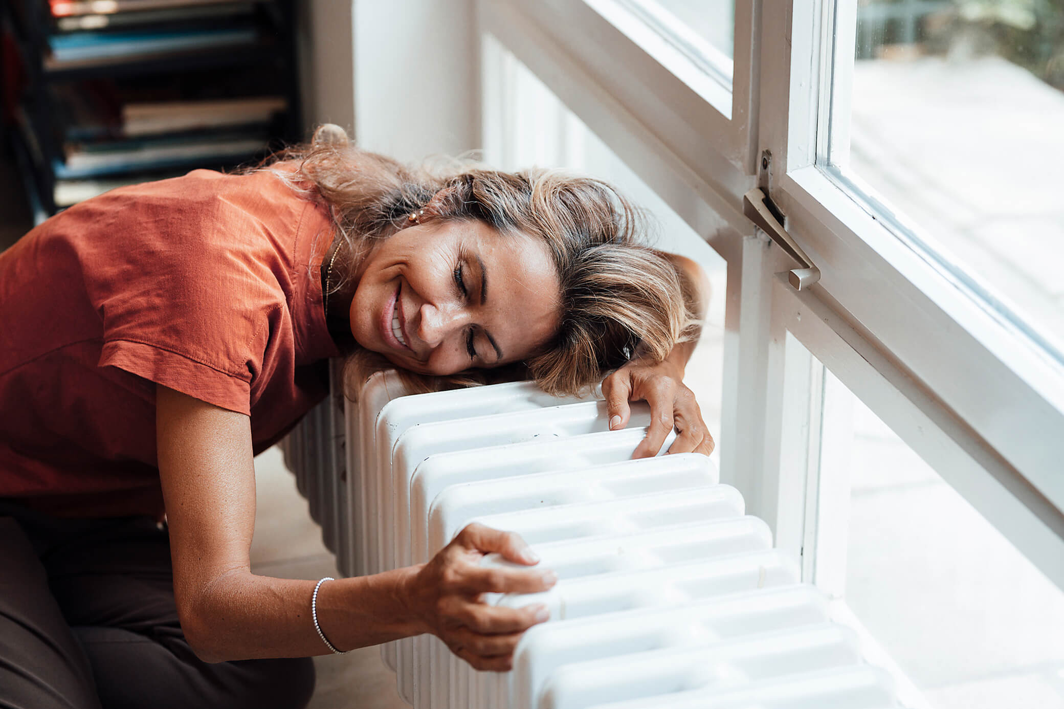 Heiz dein Zuhause mit Energie aus der Umwelt - klimafreundlich Frau am Fenster schmiegt sich an einen Heizkörper