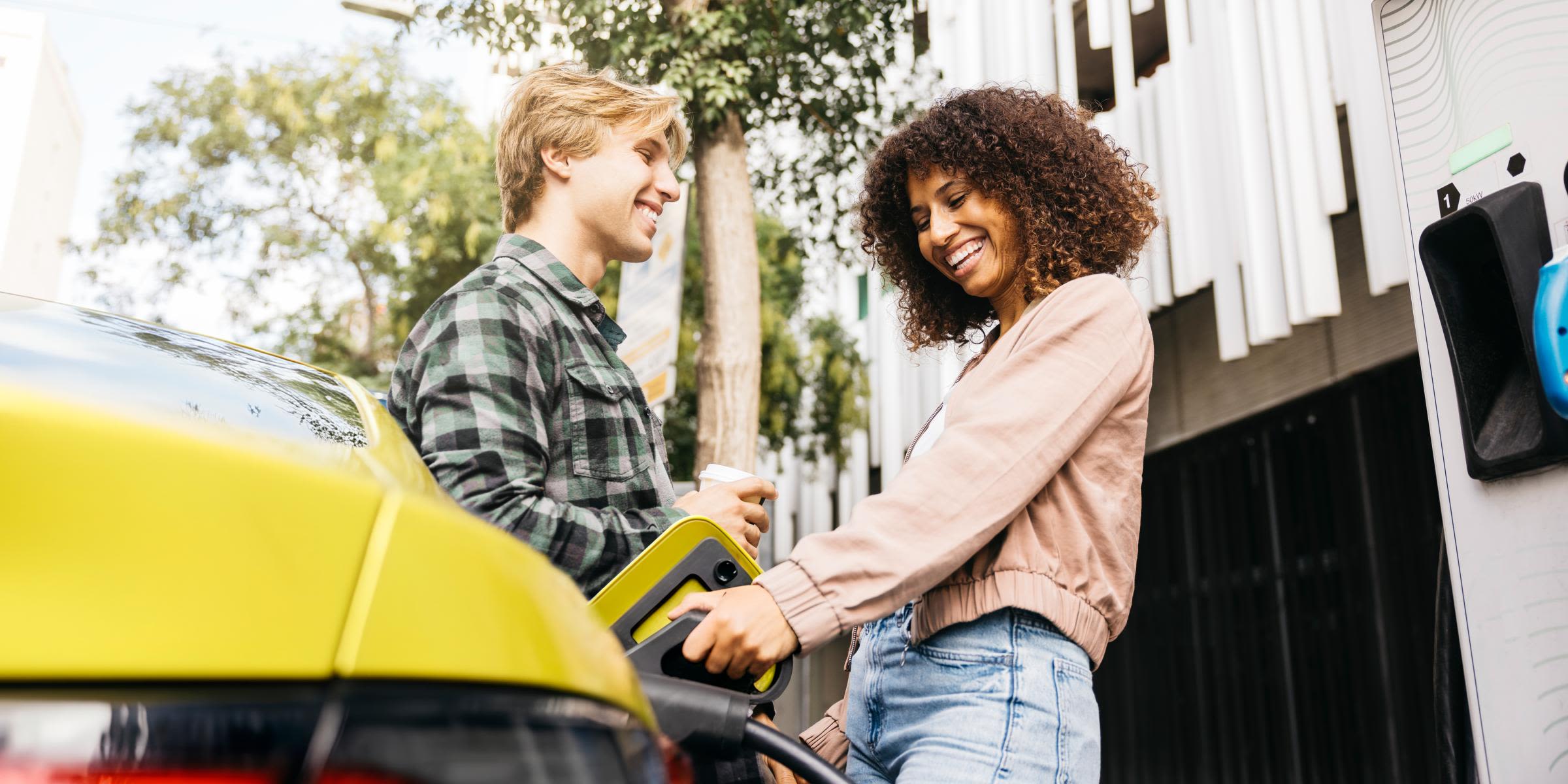 Mit der THG-Quote fährst du dein E-Auto noch günstiger Junges Paar lädt lachend ihr gelbes E-Auto in der Stadt auf