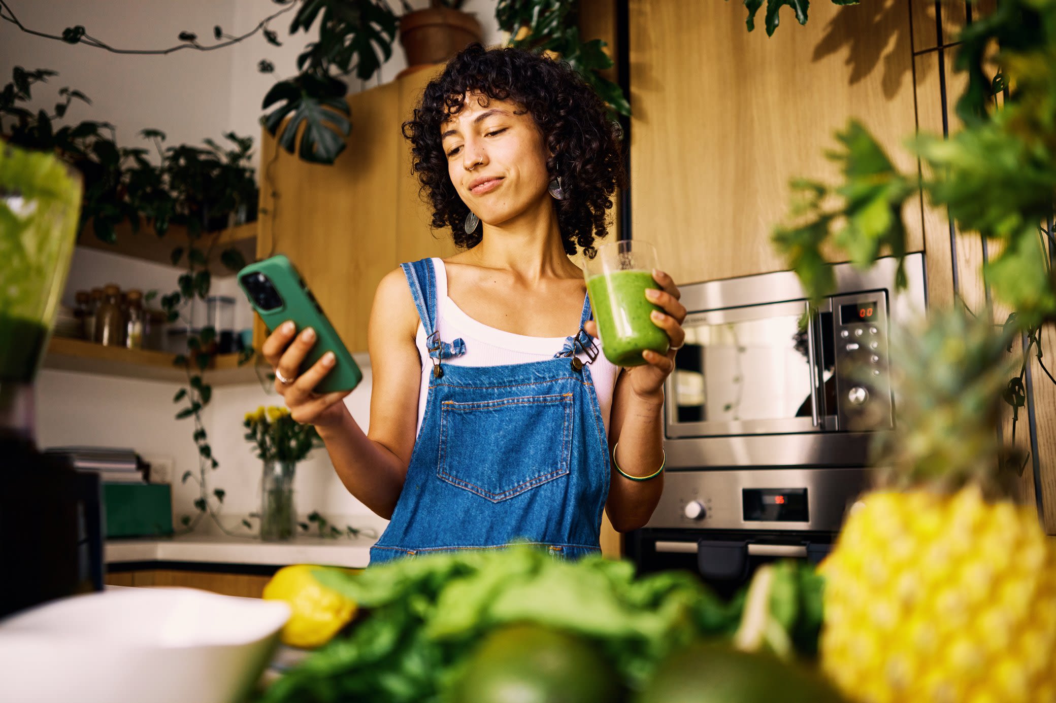 Mach dir deinen eigenen Strommix - am besten grün Frau mit Smoothie in der Hand steht in der Küche und schaut auf ihr Smartphone