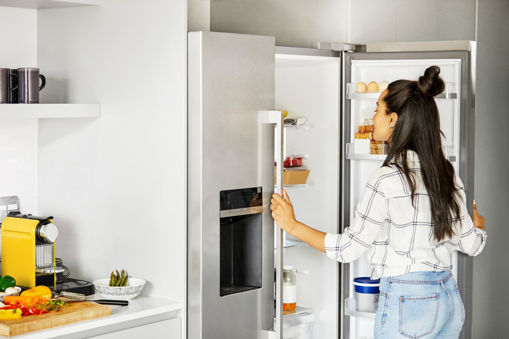 Ein energieeffizienter Kühlschrank spart viel Strom Junge Frau öffnet energieeffizienten Kühlschrank