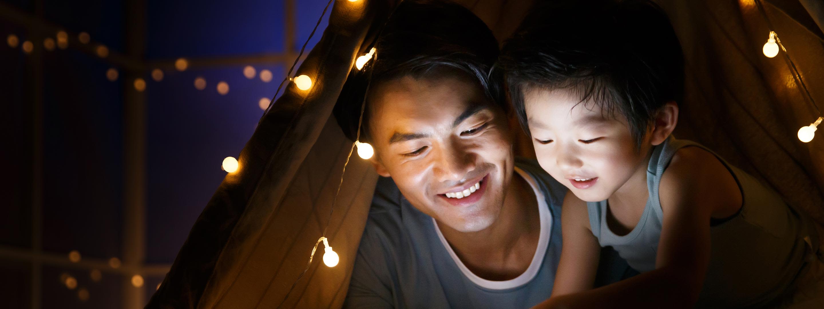 Der Strom ist ausgefallen? So verhältst du dich richtig. Vater und Sohn lesen abends bei wenig Licht ein Buch