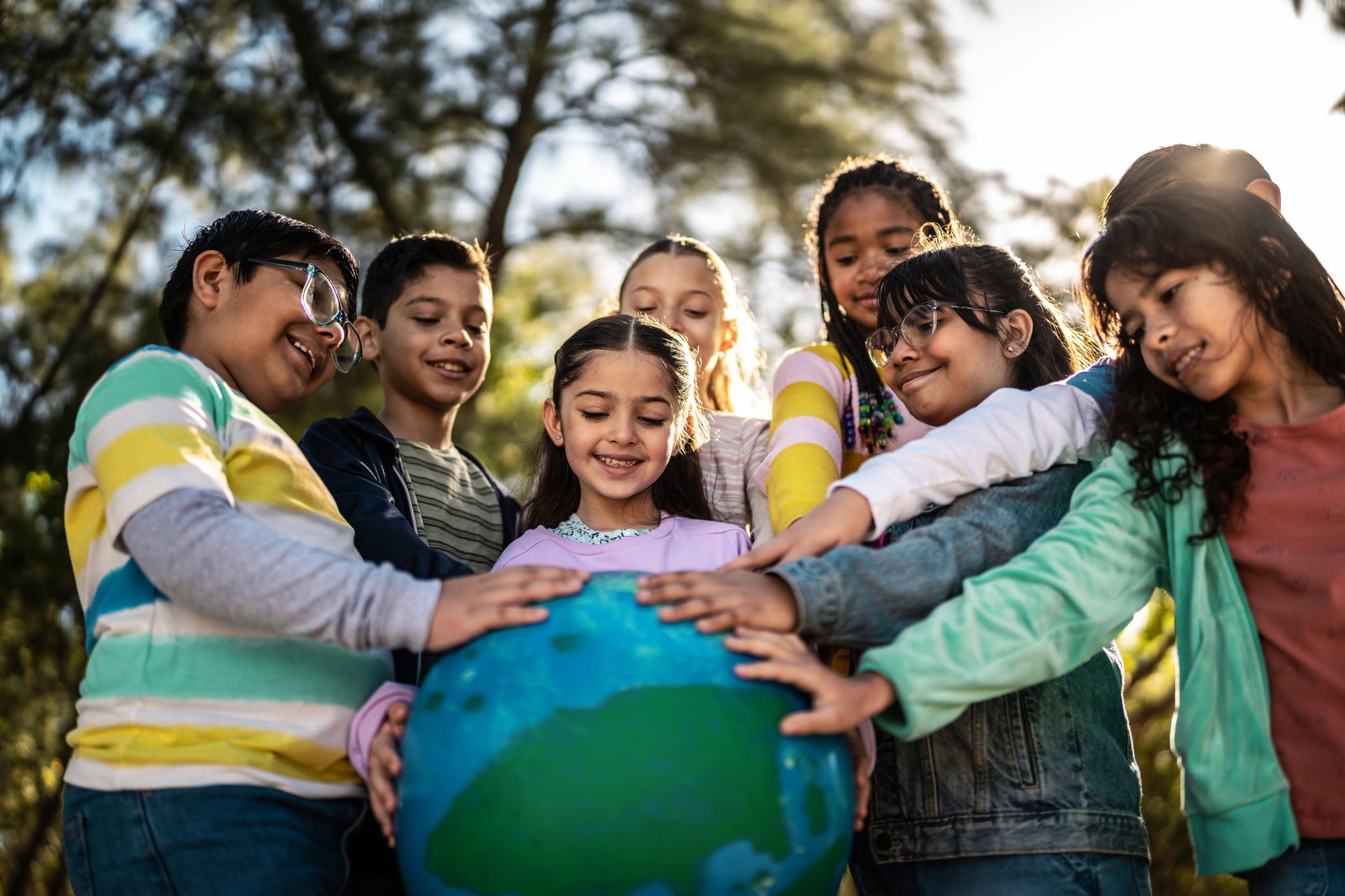 Klimaschutz geht uns alle an, denn die Erde teilen wir uns Kinder stehen im Kreis und berühren lächelnd eine Erde aus Pappe
