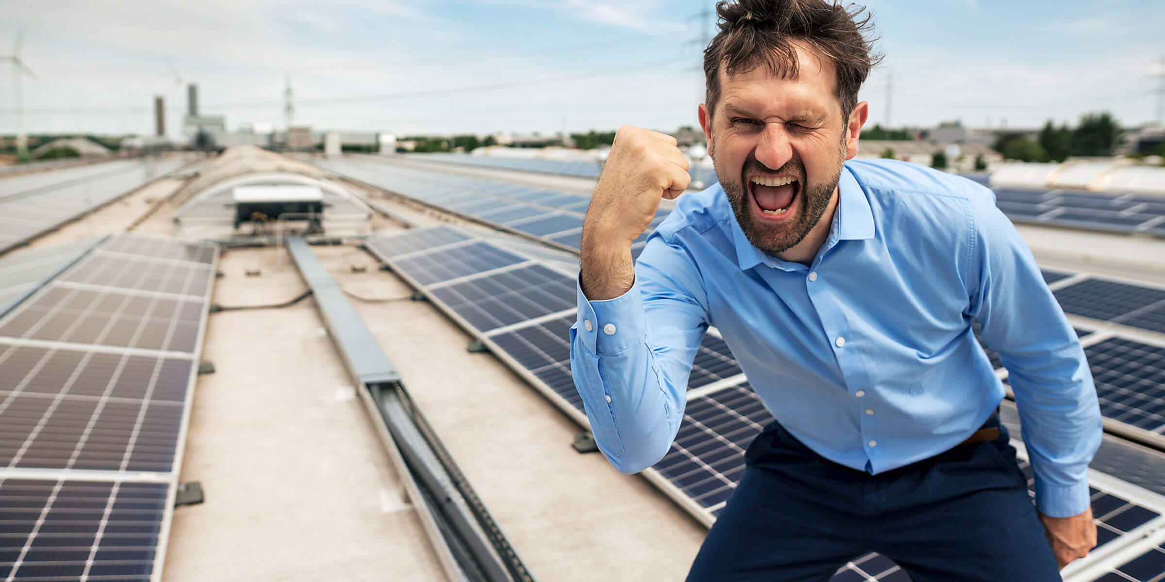 Ein Mann steht jubelnd auf einem Solar Dach.